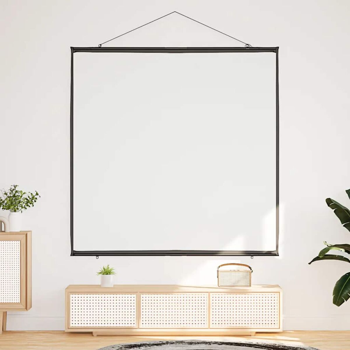 Eine weiße Projektorleinwand hängt an einem schwarzen Rahmen. Ein Holzschrank und eine Pflanze darunter, weiße Wand.