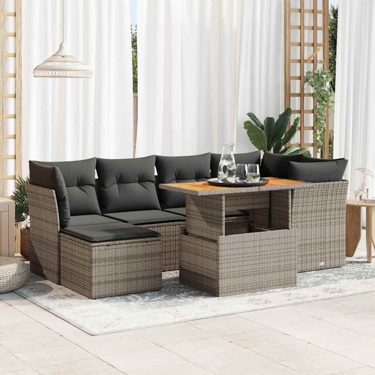 Set divano in rattan da esterno con tavolo, cuscini e tende sullo sfondo.