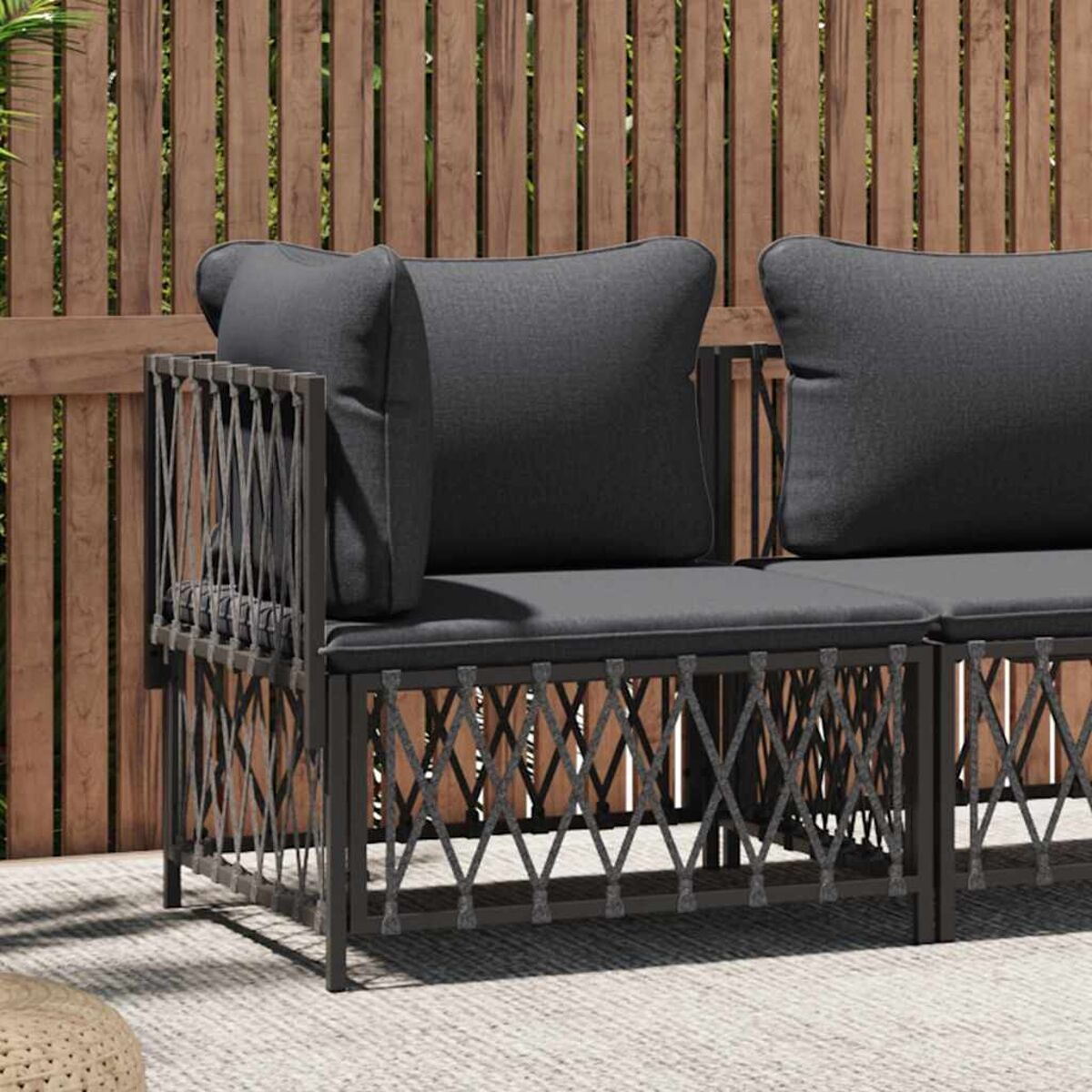 Graues Outdoor-Sofa mit dunkelgrauen Kissen. Holzzaun im Hintergrund. Sonniger Tag.