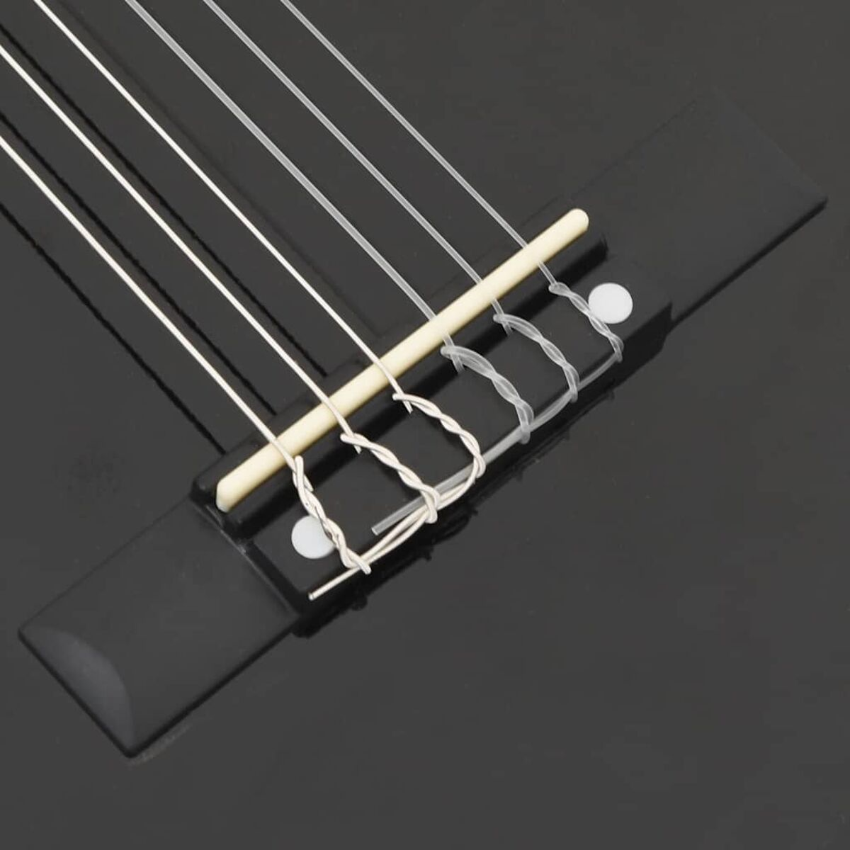 Nahaufnahme einer schwarzen Gitarrenbrücke mit weißen Saiten.