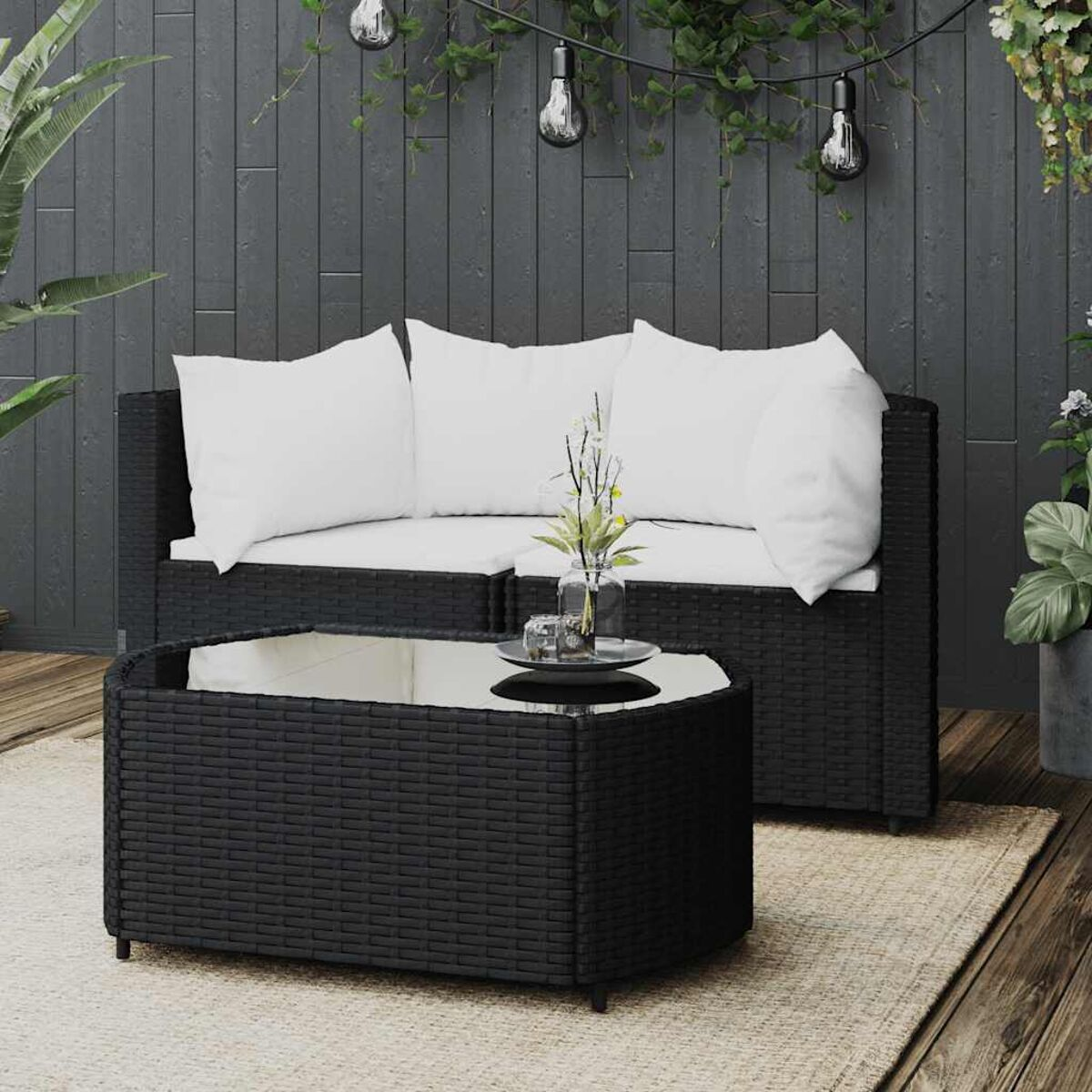 Schwarzes Outdoor-Sitzmöbelset aus Korbgeflecht mit einem Couchtisch mit Glasplatte und weißen Kissen.