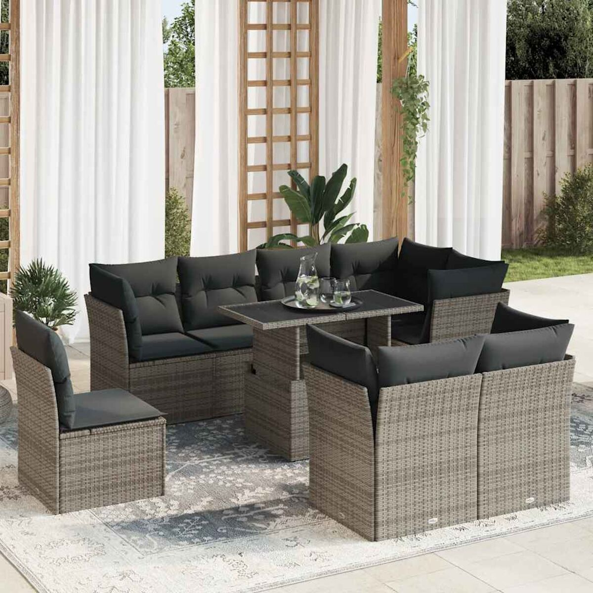 Set di sedute da esterno in rattan grigio con tavolo, cuscini, tende e schermo decorativo in legno.