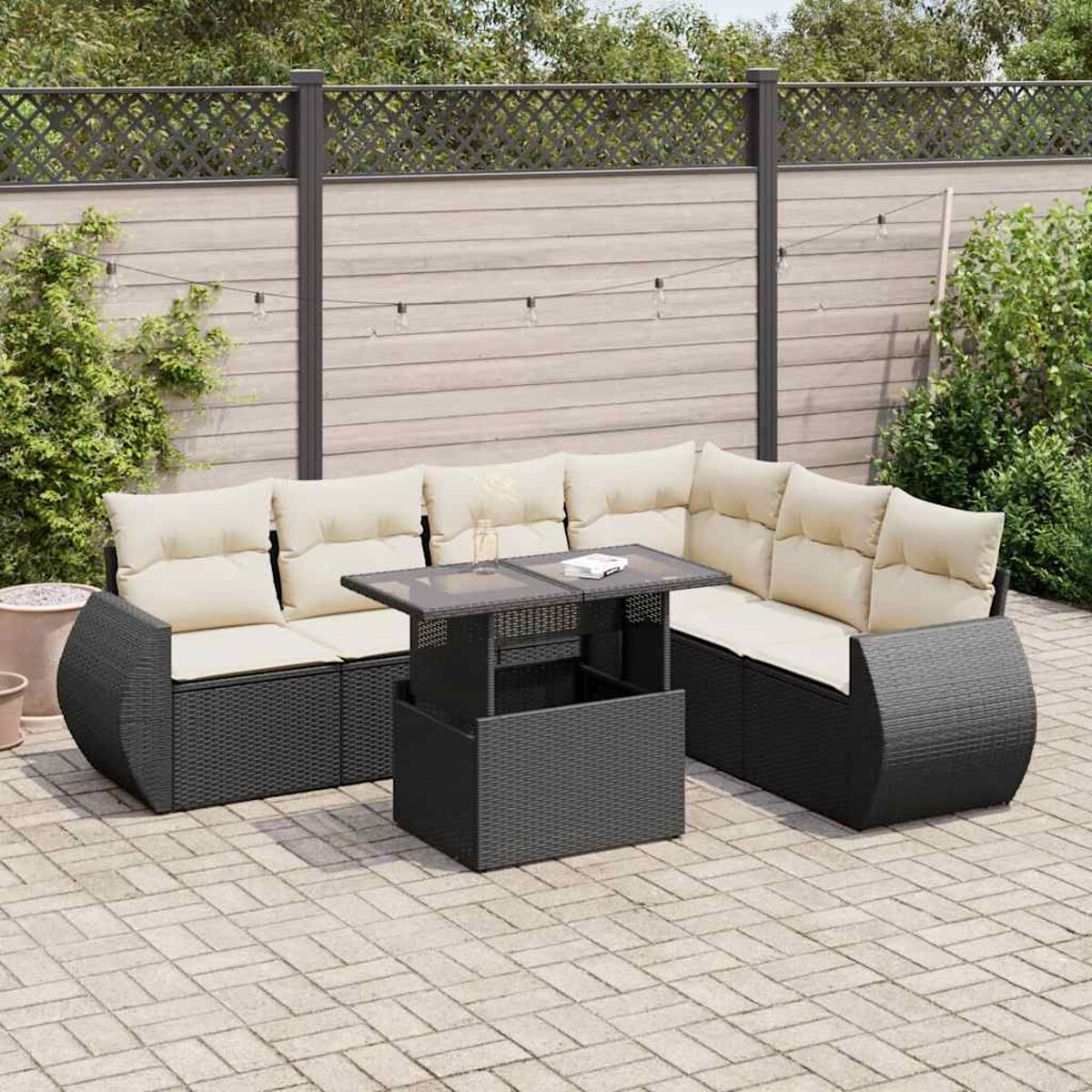 Set patio in vimini nero con cuscini chiari, un tavolo e luci a corda sopra.