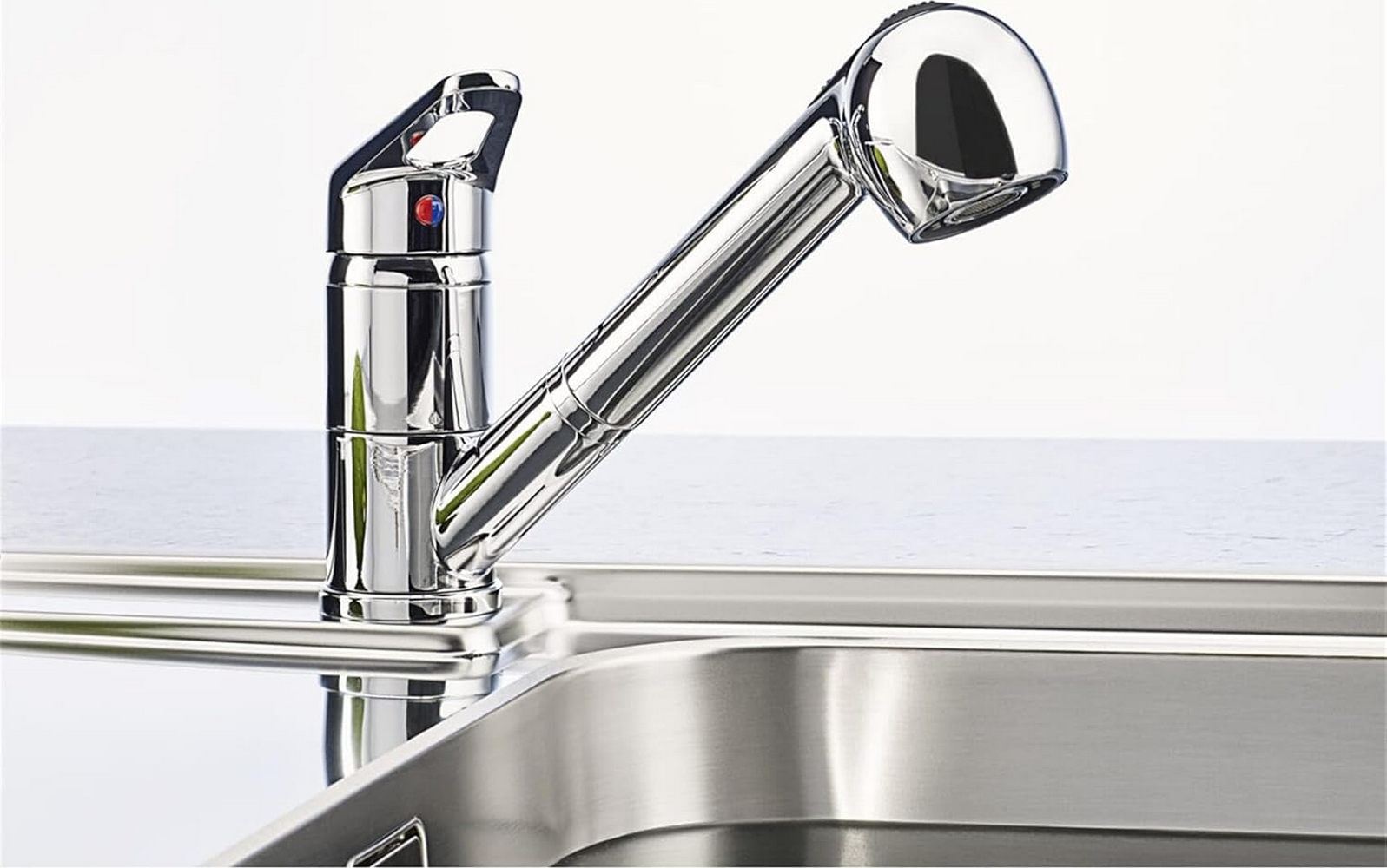 Rubinetto da cucina argentato con doccetta estraibile. Su lavello in metallo, sfondo bianco.