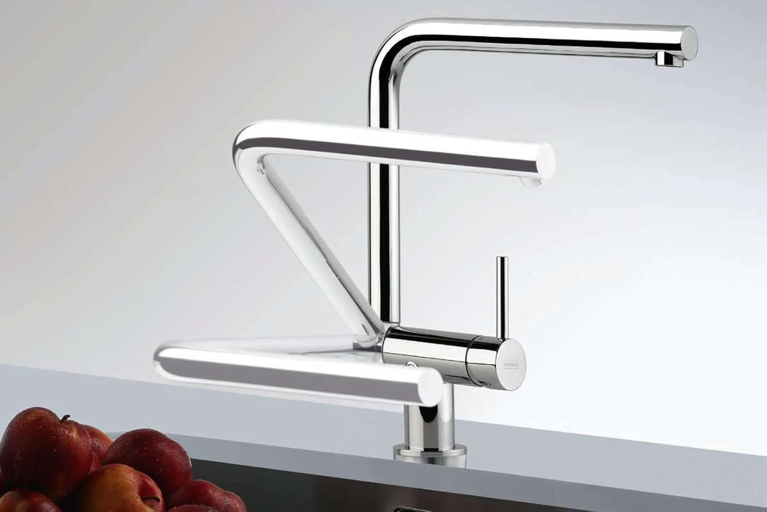 Un rubinetto da cucina cromato con un design unico. Mele rosse in primo piano su un piano di lavoro.