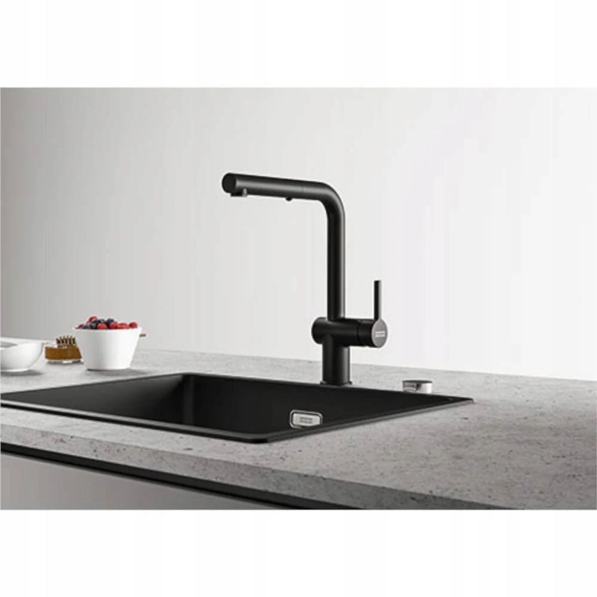Rubinetto da cucina nero sopra un lavandino nero su un piano di lavoro grigio chiaro. Sfondo bianco.
