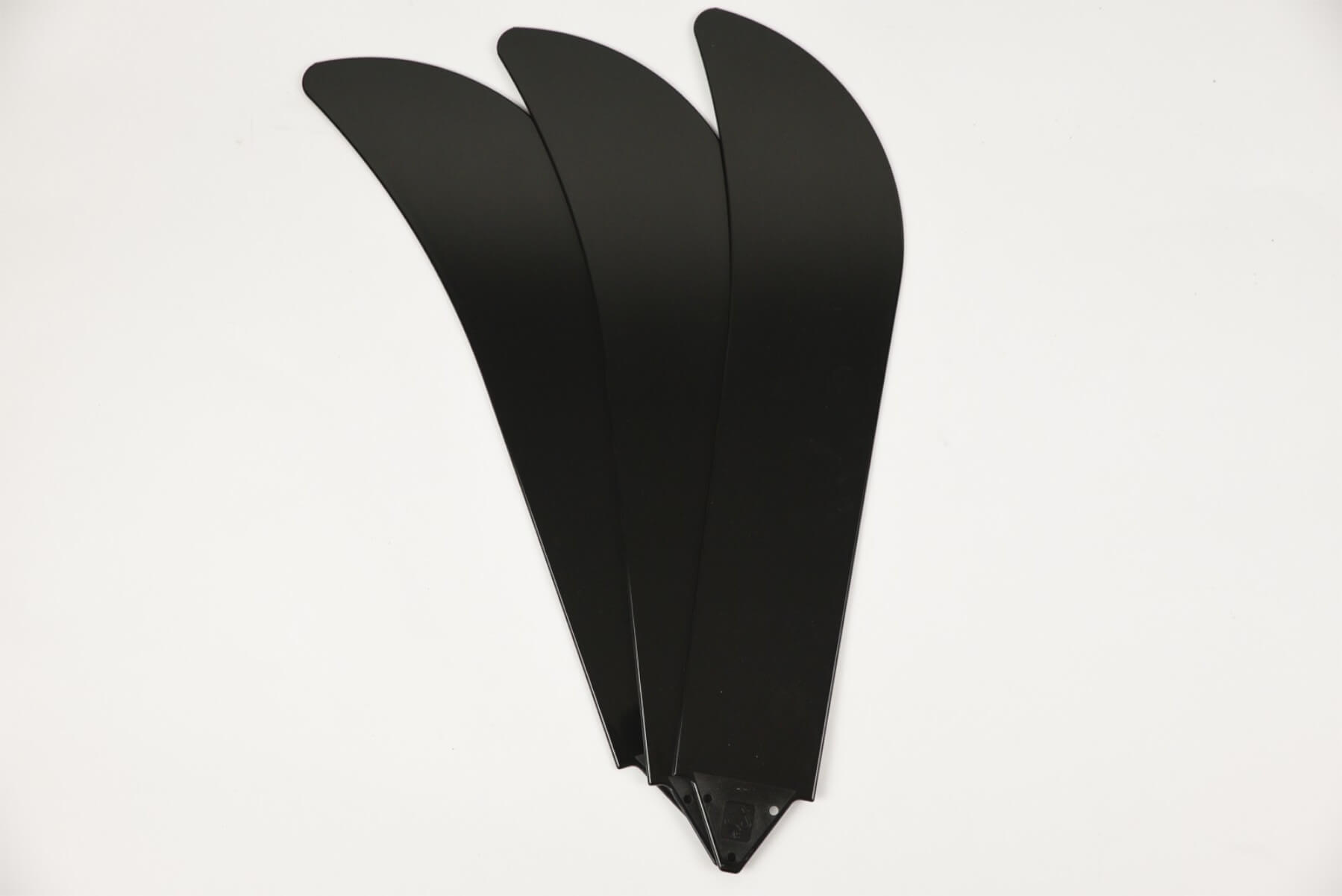 Drei schwarze Deckenventilatorflügel, angeordnet auf einer weißen Oberfläche.