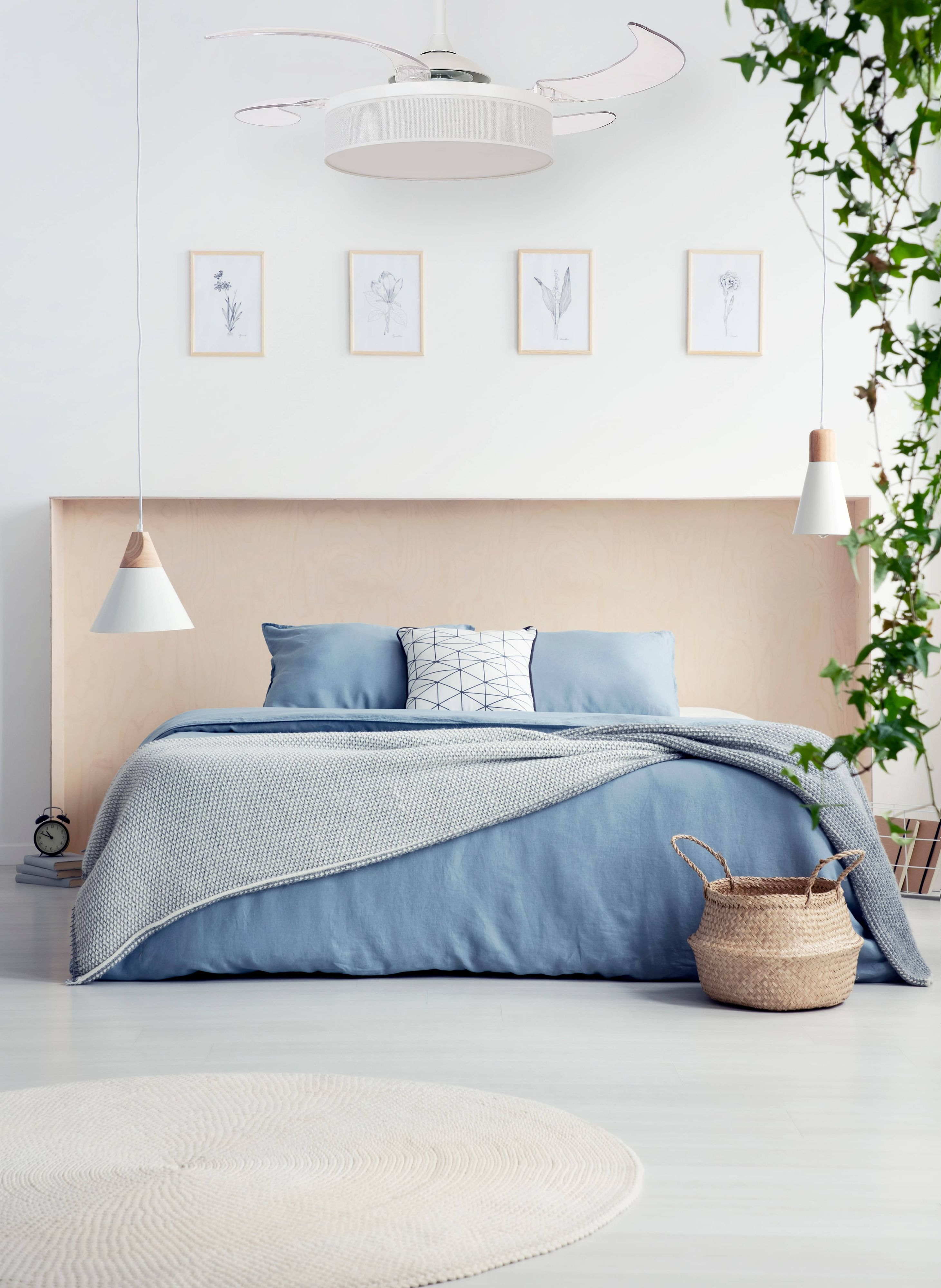 Ein Schlafzimmer mit Bett, blauer Bettwäsche und einem geflochtenen Korb. Ein Ventilator und Kunstwerke hängen.