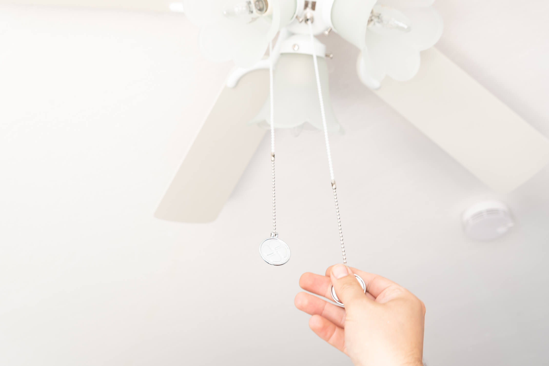 Una mano tira una catena per accendere un ventilatore da soffitto bianco con quattro pale.