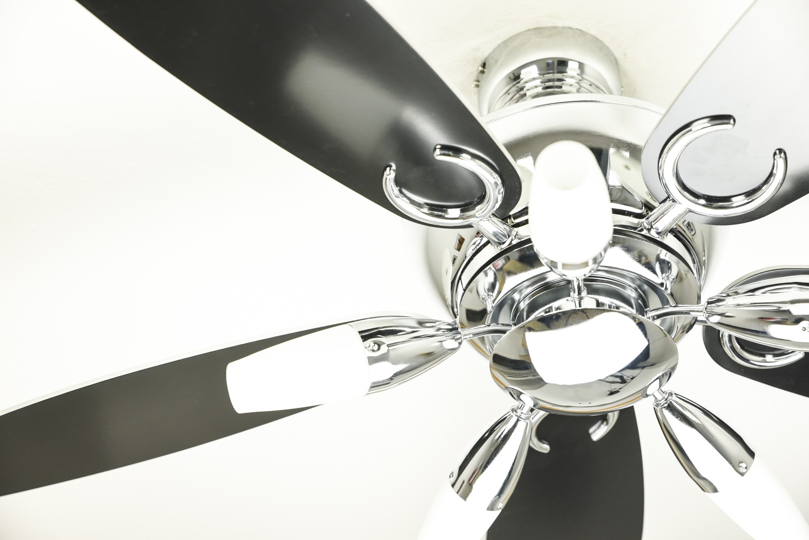 Deckenventilator von unten, schwarze Flügel, Chromakzente, weißer Deckenhintergrund.