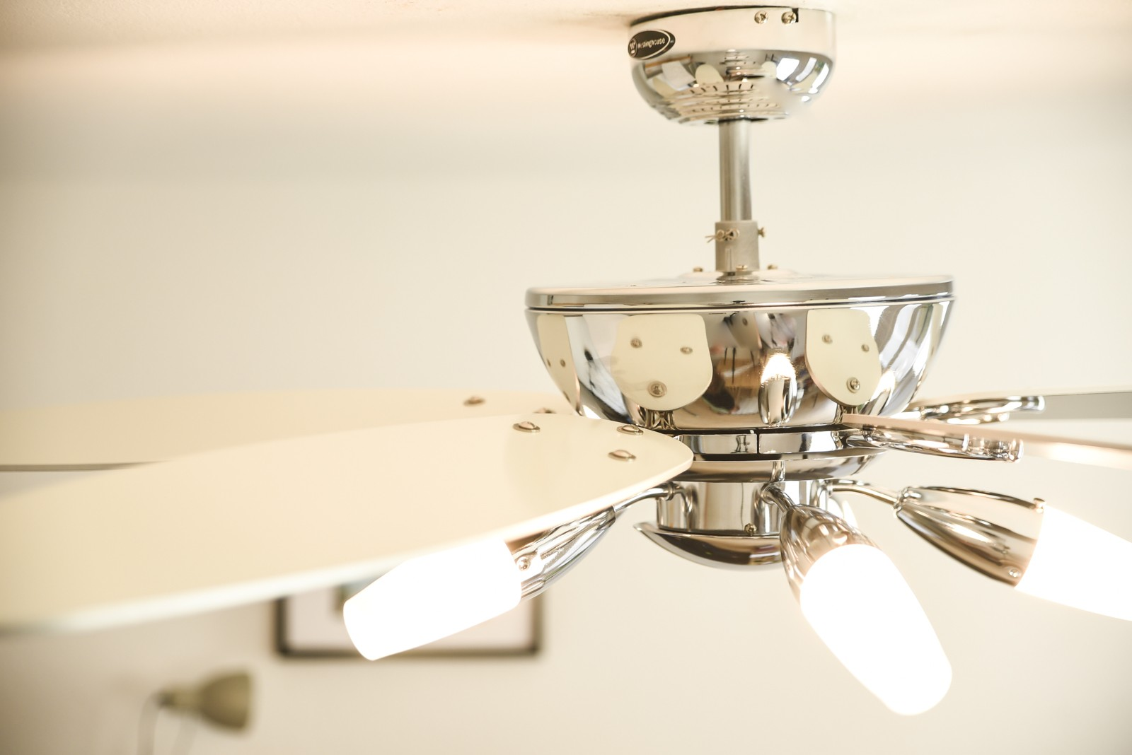 Silberner Deckenventilator mit Lichtern, weißen Flügeln und heller Decke.