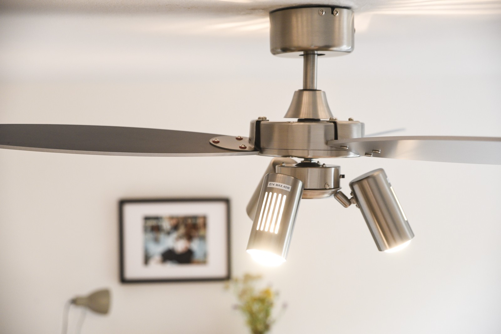 Deckenventilator mit drei Strahlern, die den Vordergrund beleuchten. Bild an der Wand.
