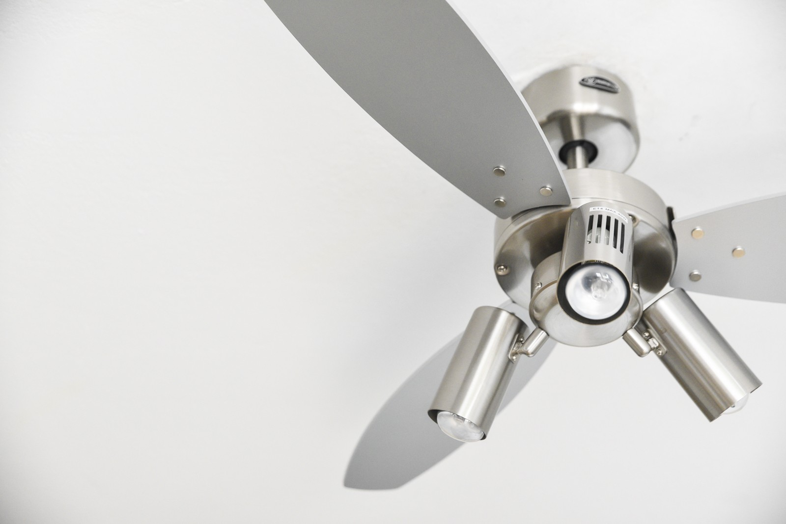 Silberner Deckenventilator mit drei Flügeln und Lichtern. Weißer Deckenhintergrund.