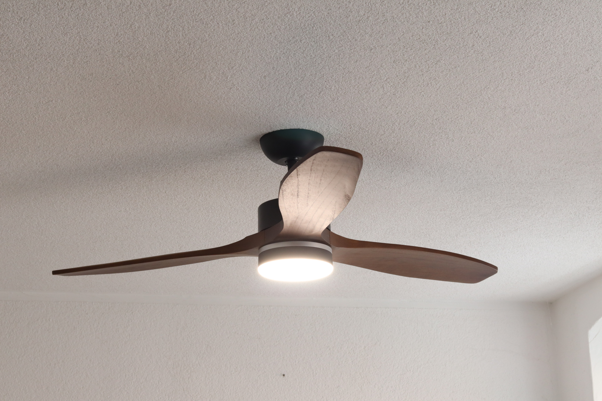 Deckenventilator mit drei Holzblättern, Licht und dunklem Motorgehäuse.