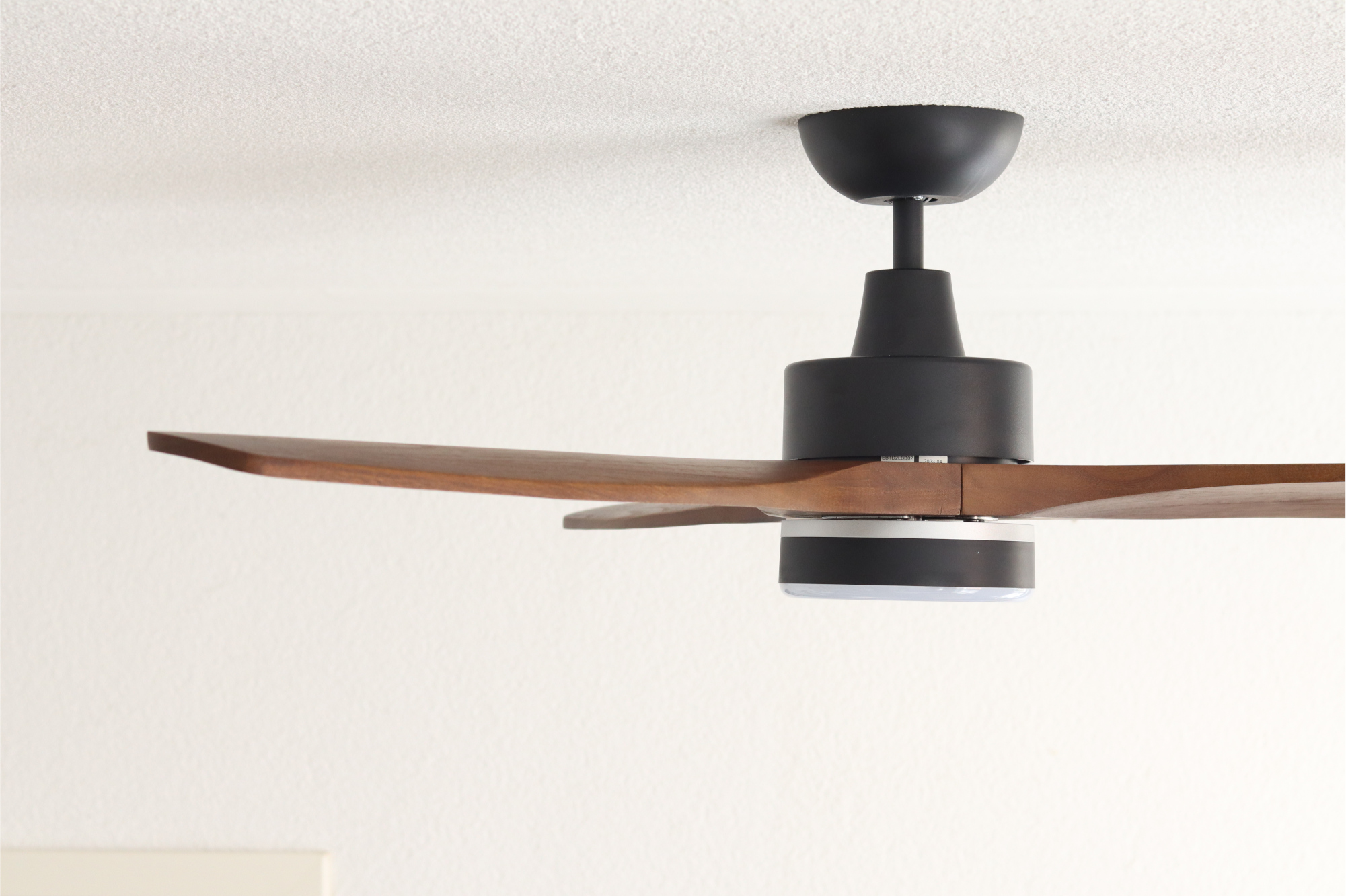 Deckenventilator mit schwarzem Motor, Holzflügeln, weißer Decke.