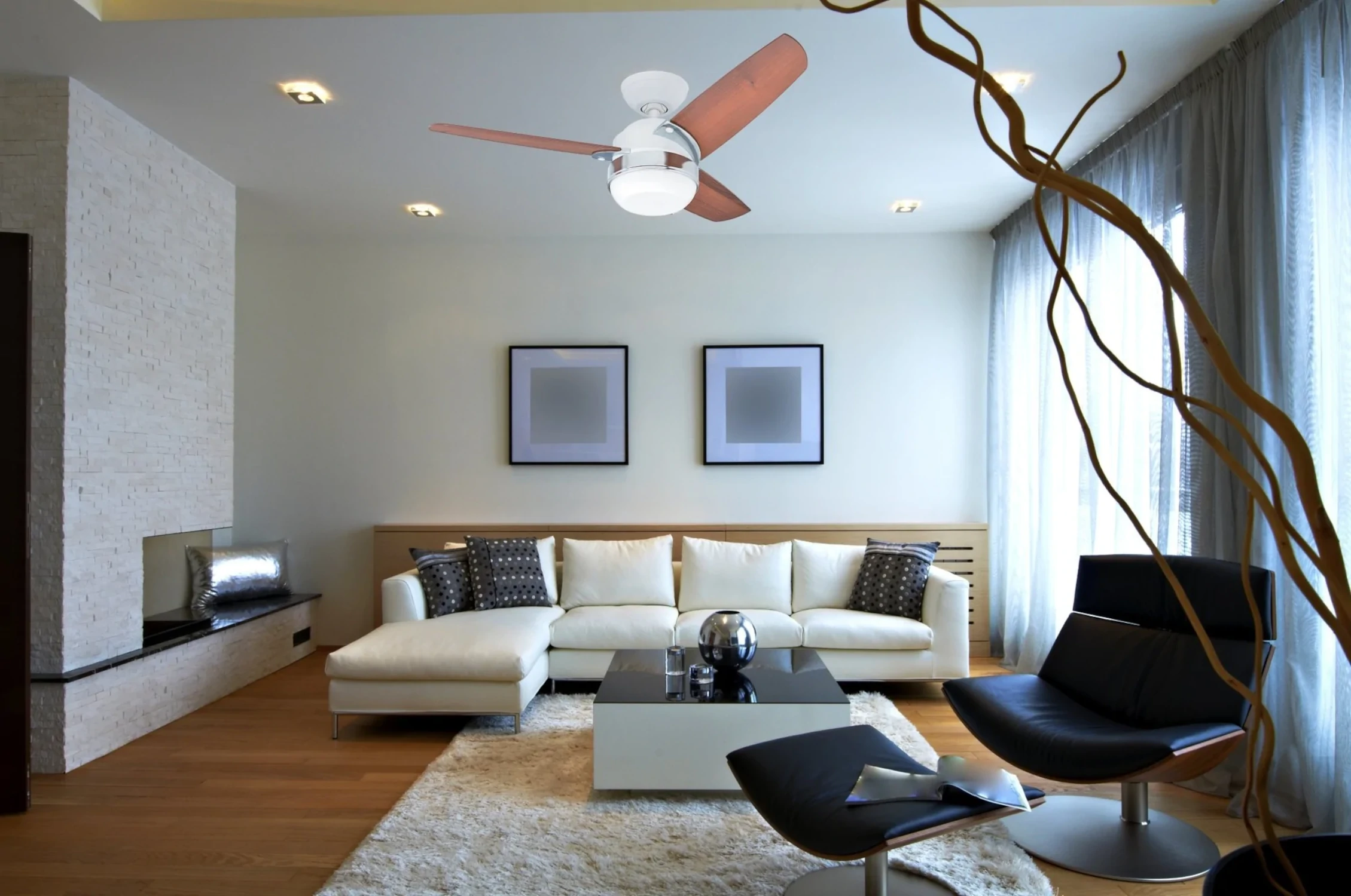 Wohnzimmer mit weißer Couch, Couchtisch und Deckenventilator. Schwarze Stühle im Raum.