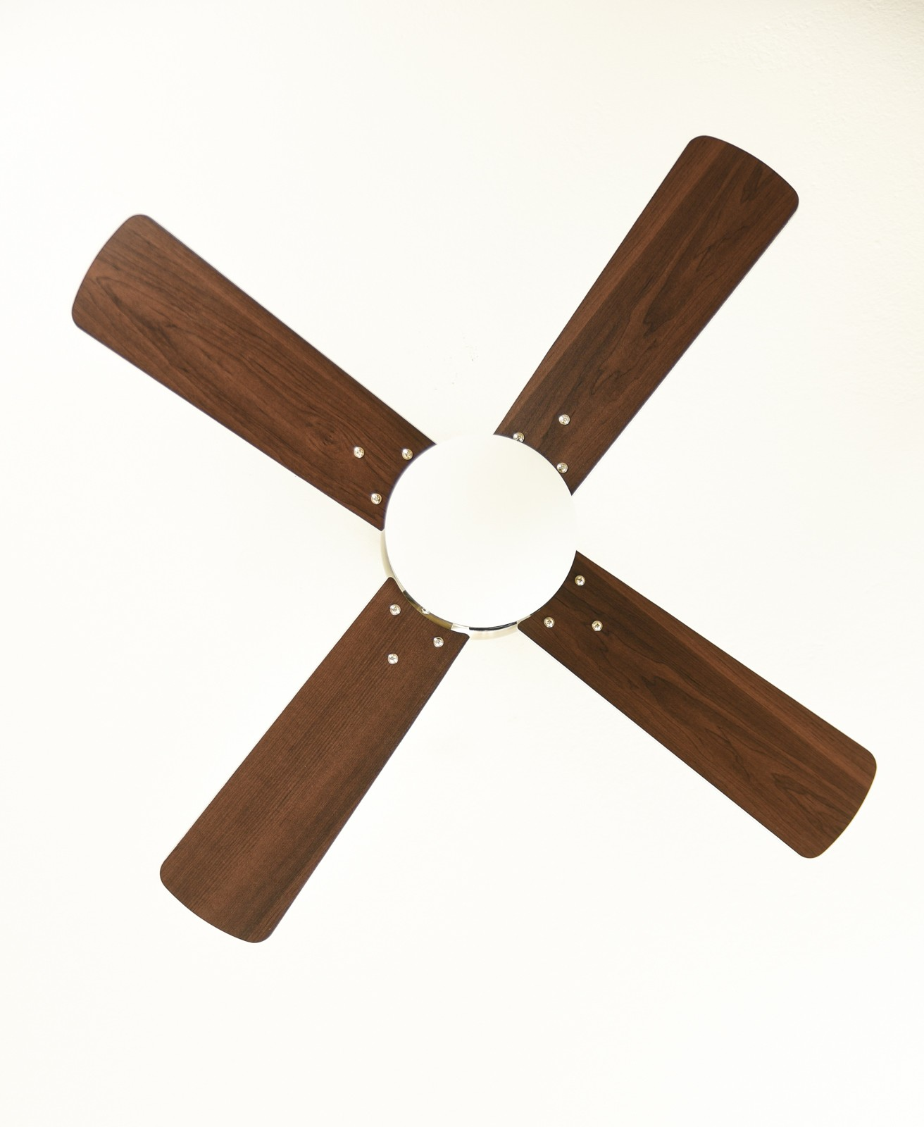 Ein Deckenventilator mit vier dunkelbraunen Flügeln, einer weißen Nabe und weißem Deckenhintergrund.