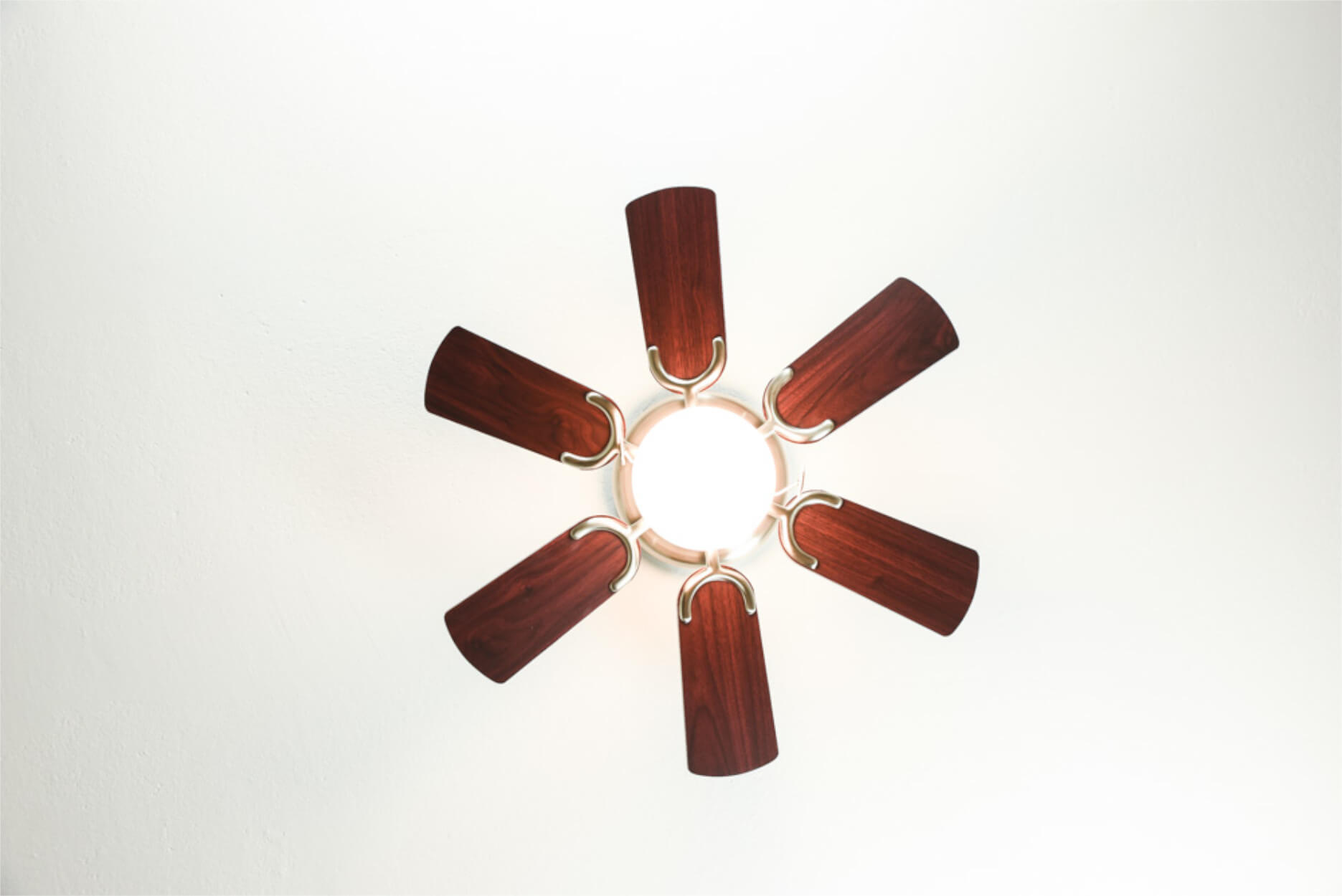 Ein Deckenventilator von unten betrachtet, mit sechs Holzblättern und einem zentralen Licht.