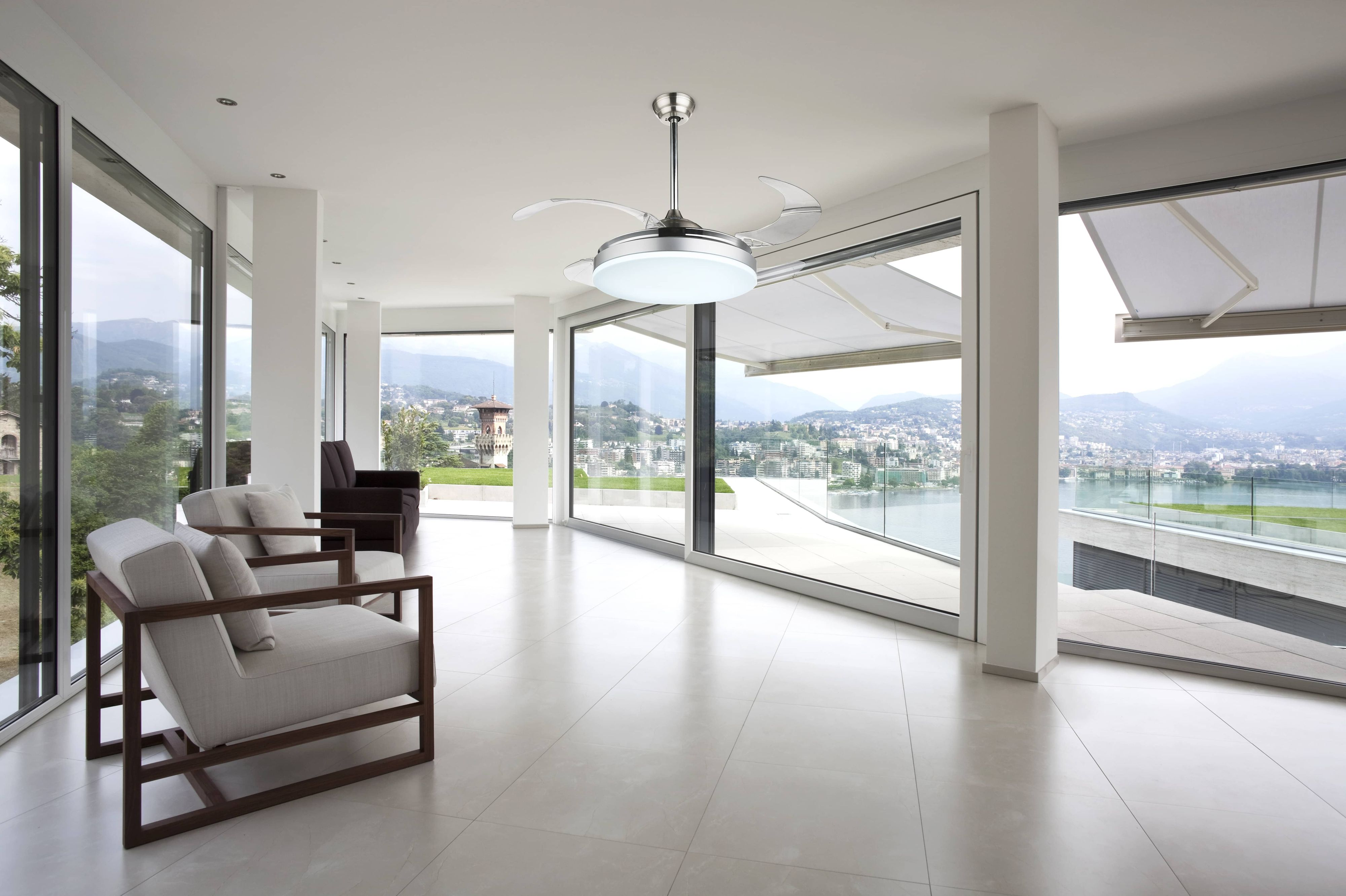 Modernes Wohnzimmer mit Deckenventilator, großen Fenstern und Blick auf Wasser und Berge.