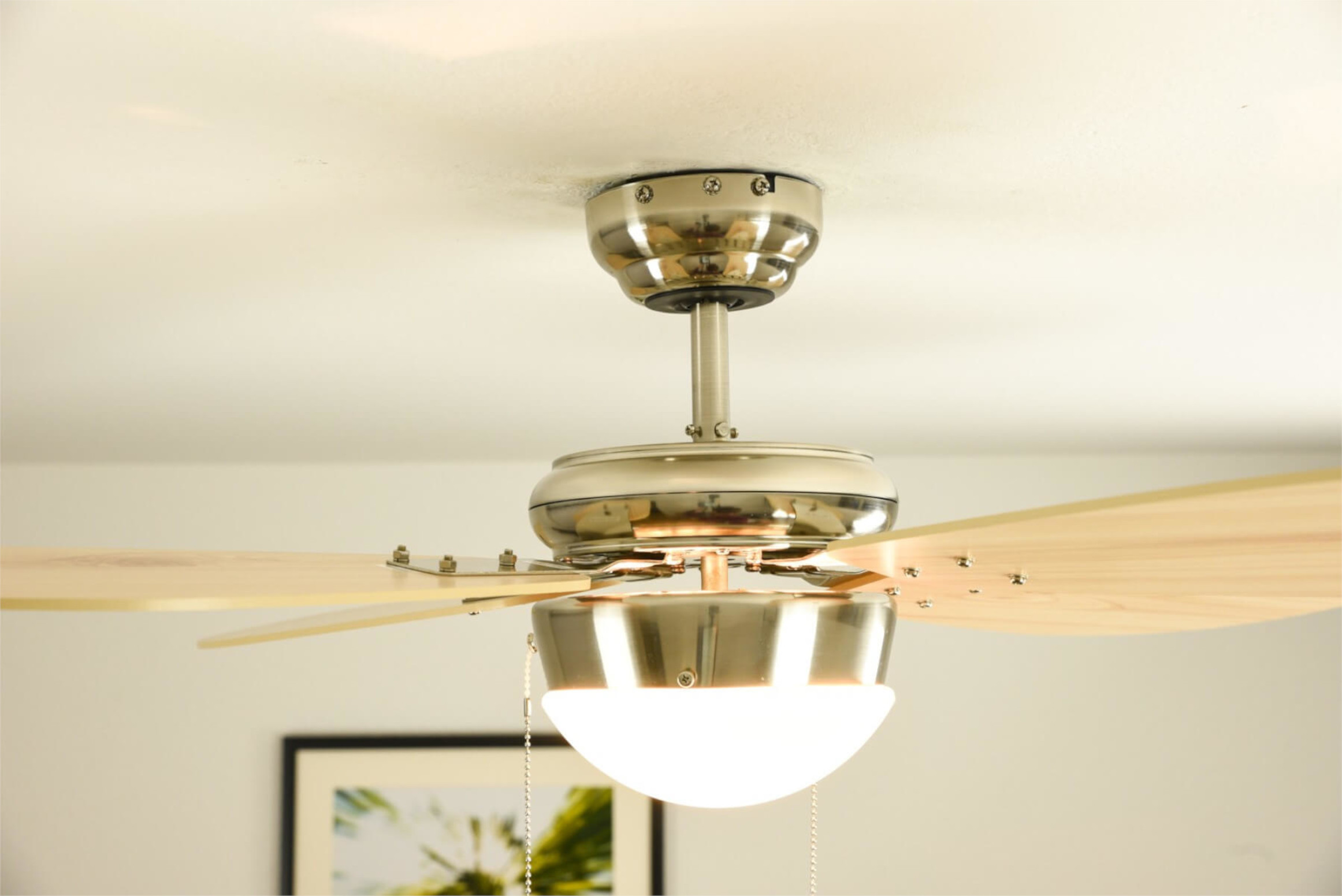 Deckenventilator mit hellen Holzflügeln, silbernem Motor und integriertem Licht.