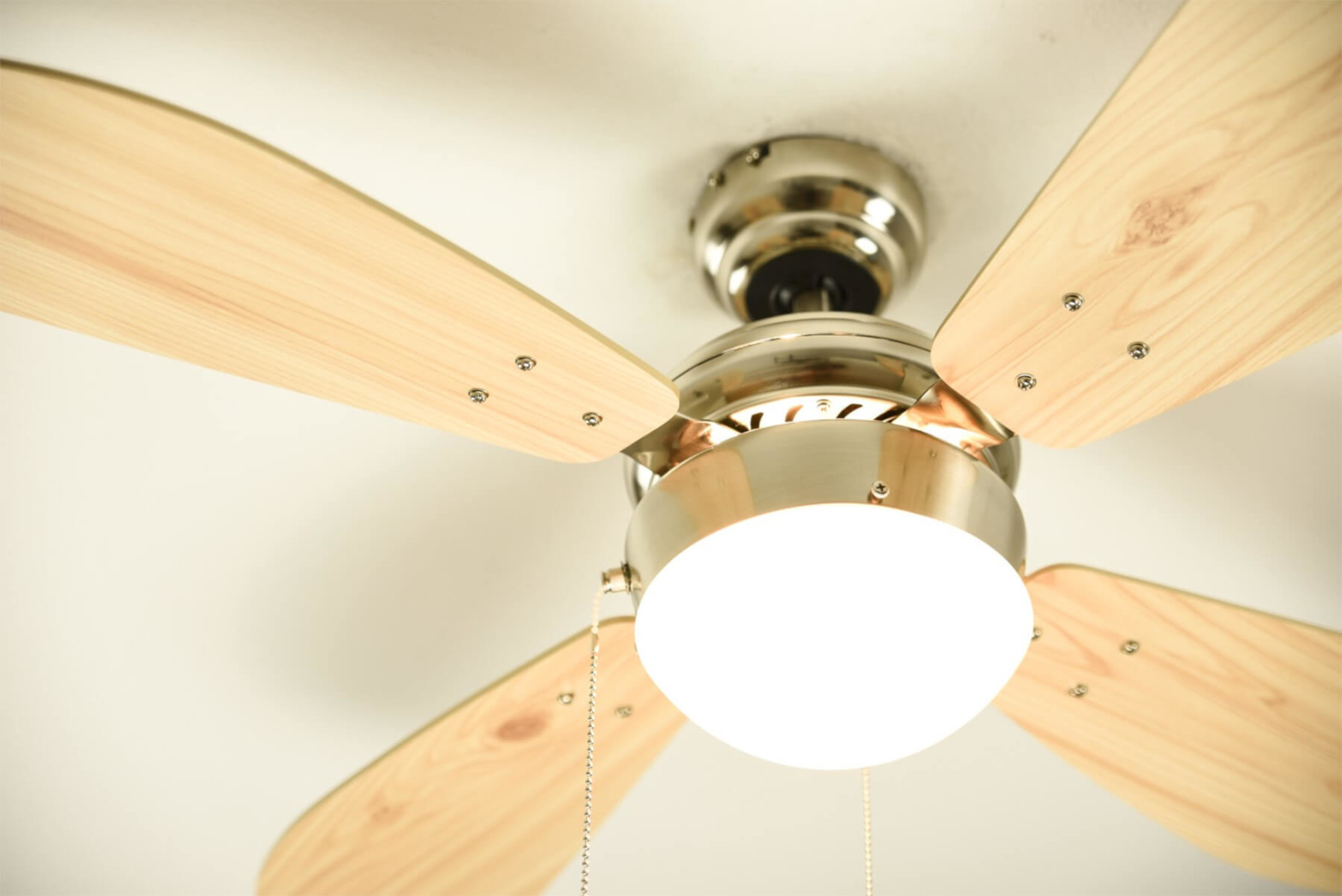 Nahaufnahme eines Deckenventilators mit Holzflügeln und einer Leuchte.