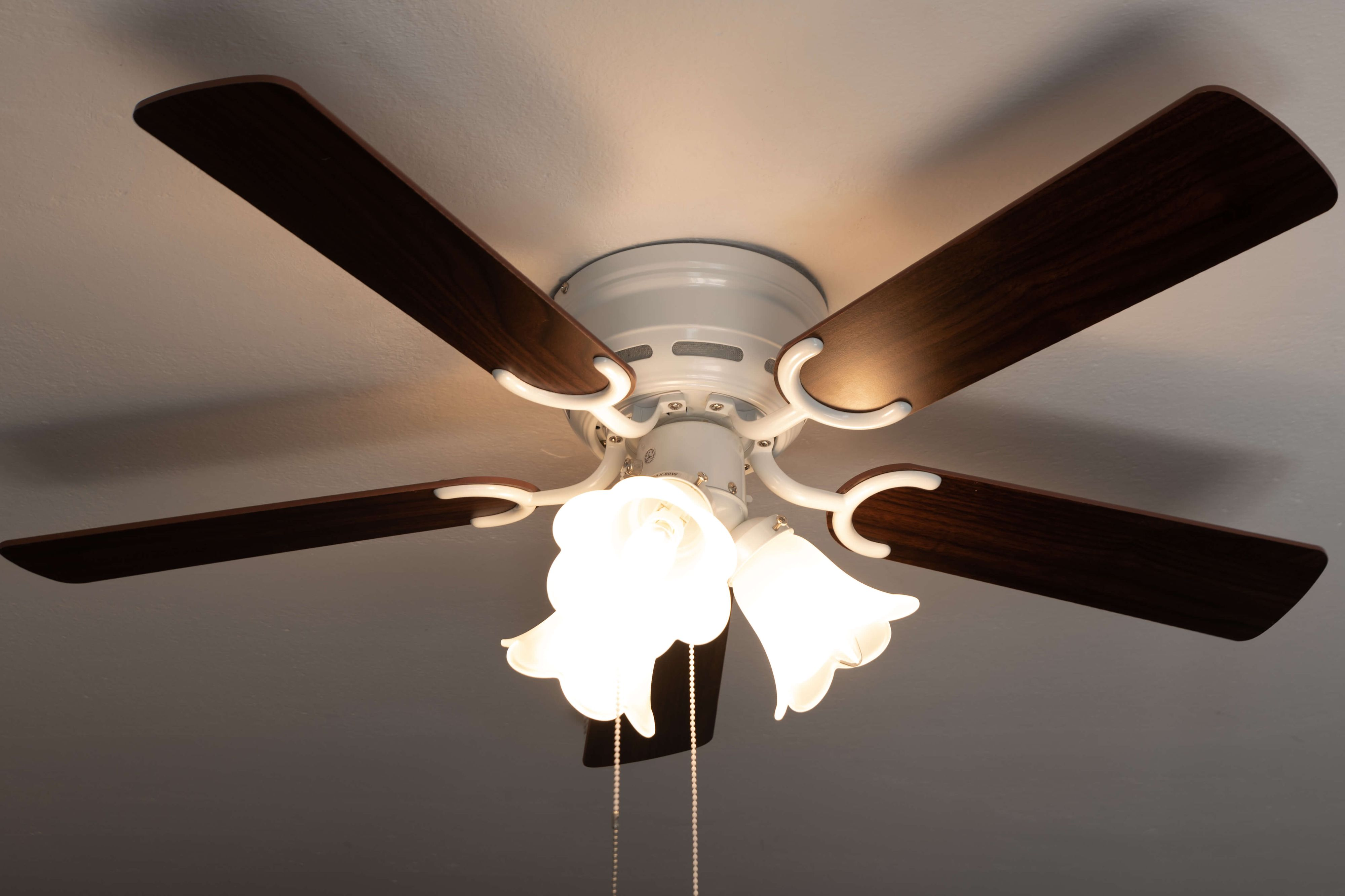 Deckenventilator mit braunen Flügeln, weißer Halterung und drei Lichtern.