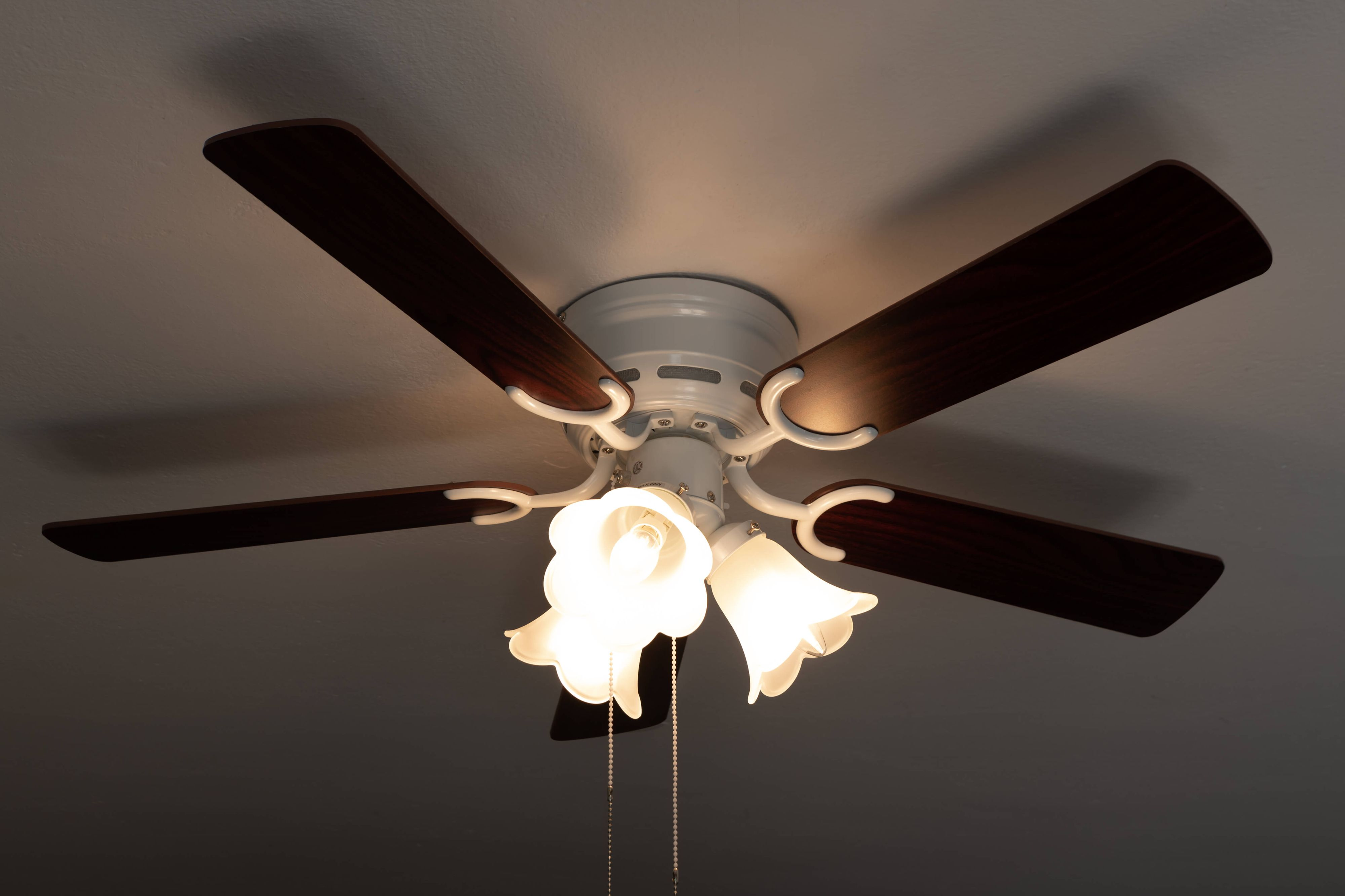 Deckenventilator mit braunen Flügeln und drei Leuchten mit Hängeketten.