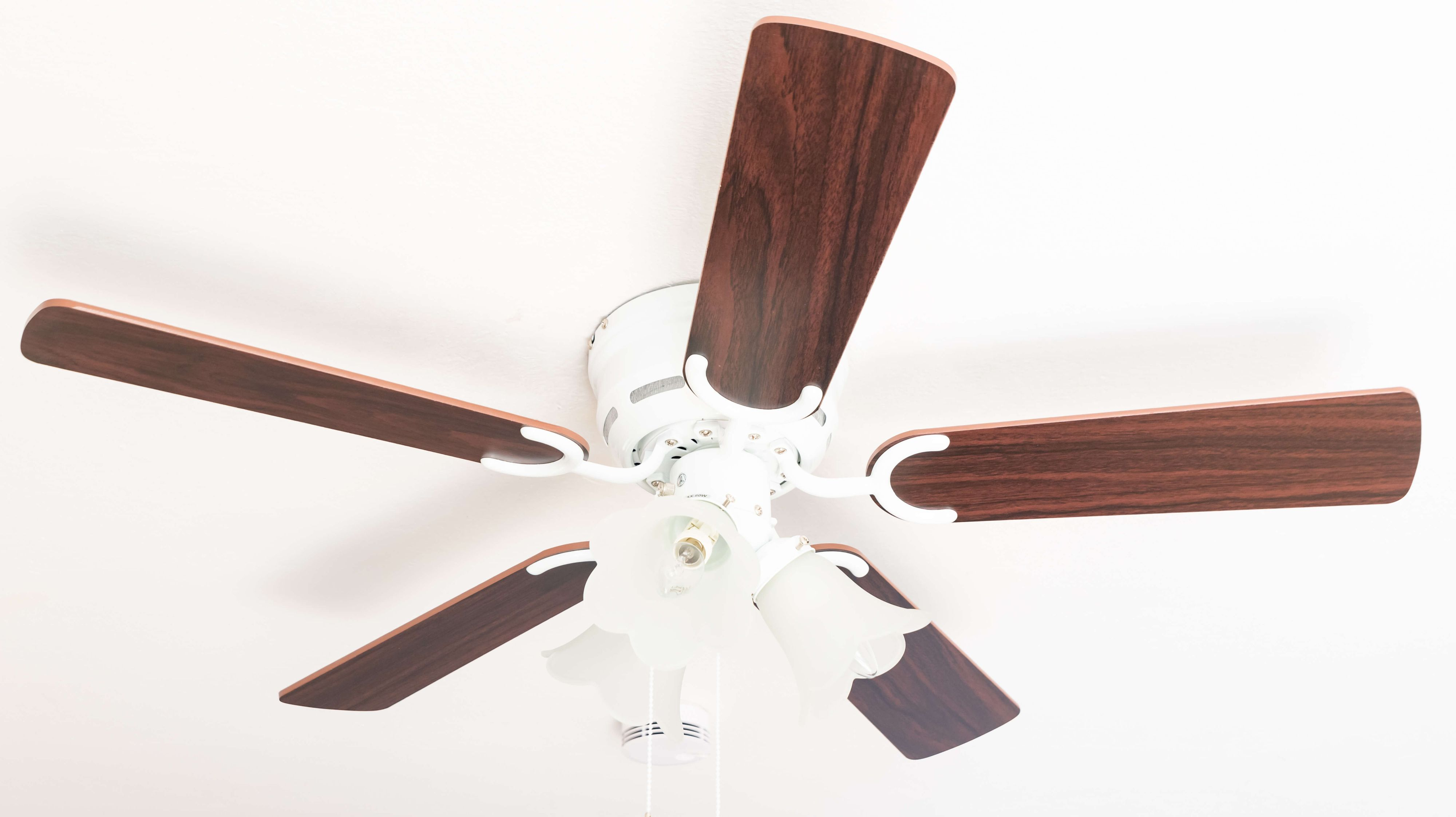 Weißer Deckenventilator mit 5 braunen Flügeln und Lichtern. Er steht vor einer weißen Decke.