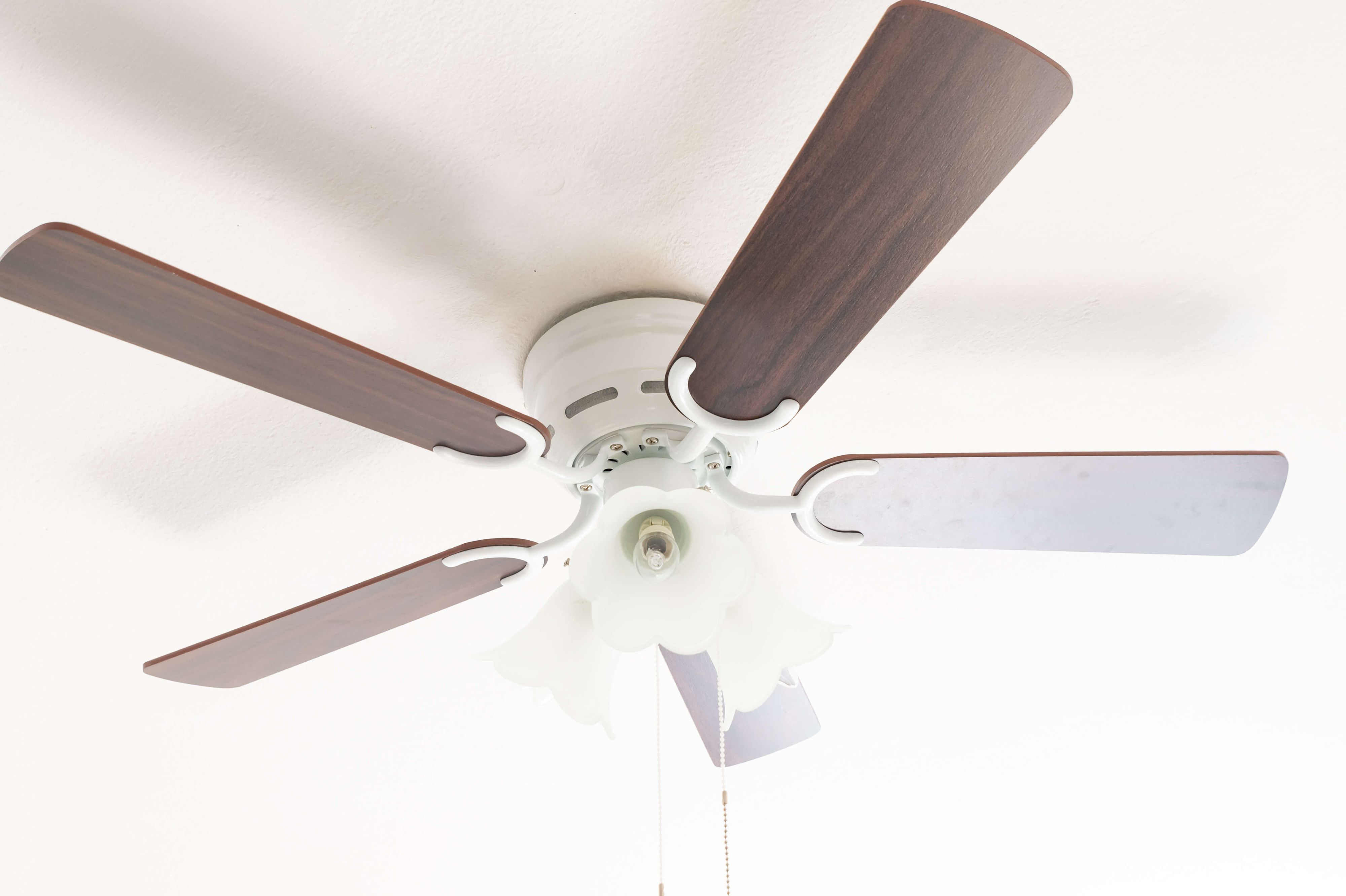 Ein Deckenventilator mit fünf Holzflügeln und weißem Sockel, der von einer weißen Decke hängt.
