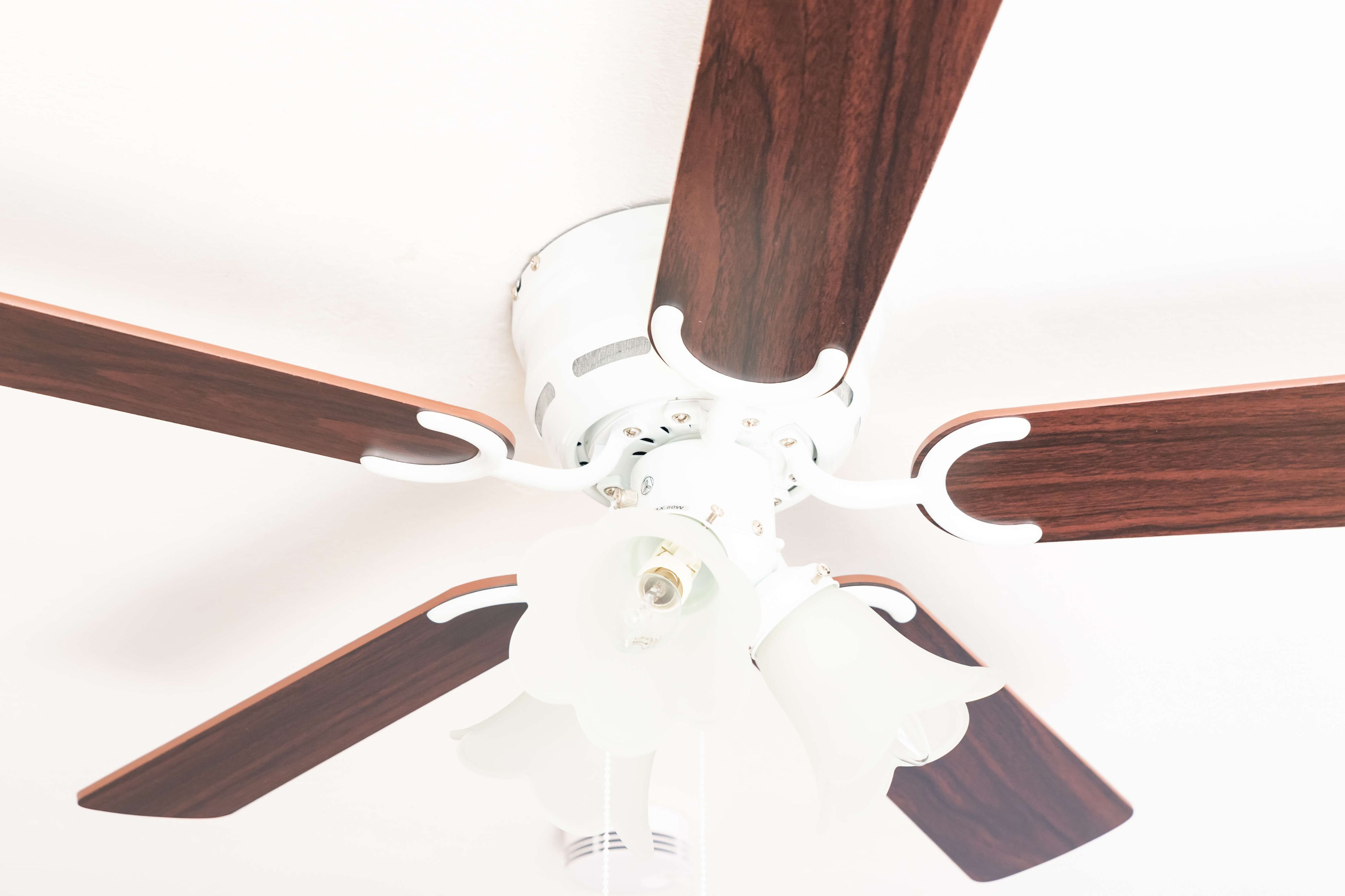 Ein Deckenventilator mit Holzflügeln und weißem Motorgehäuse, vor weißer Decke.