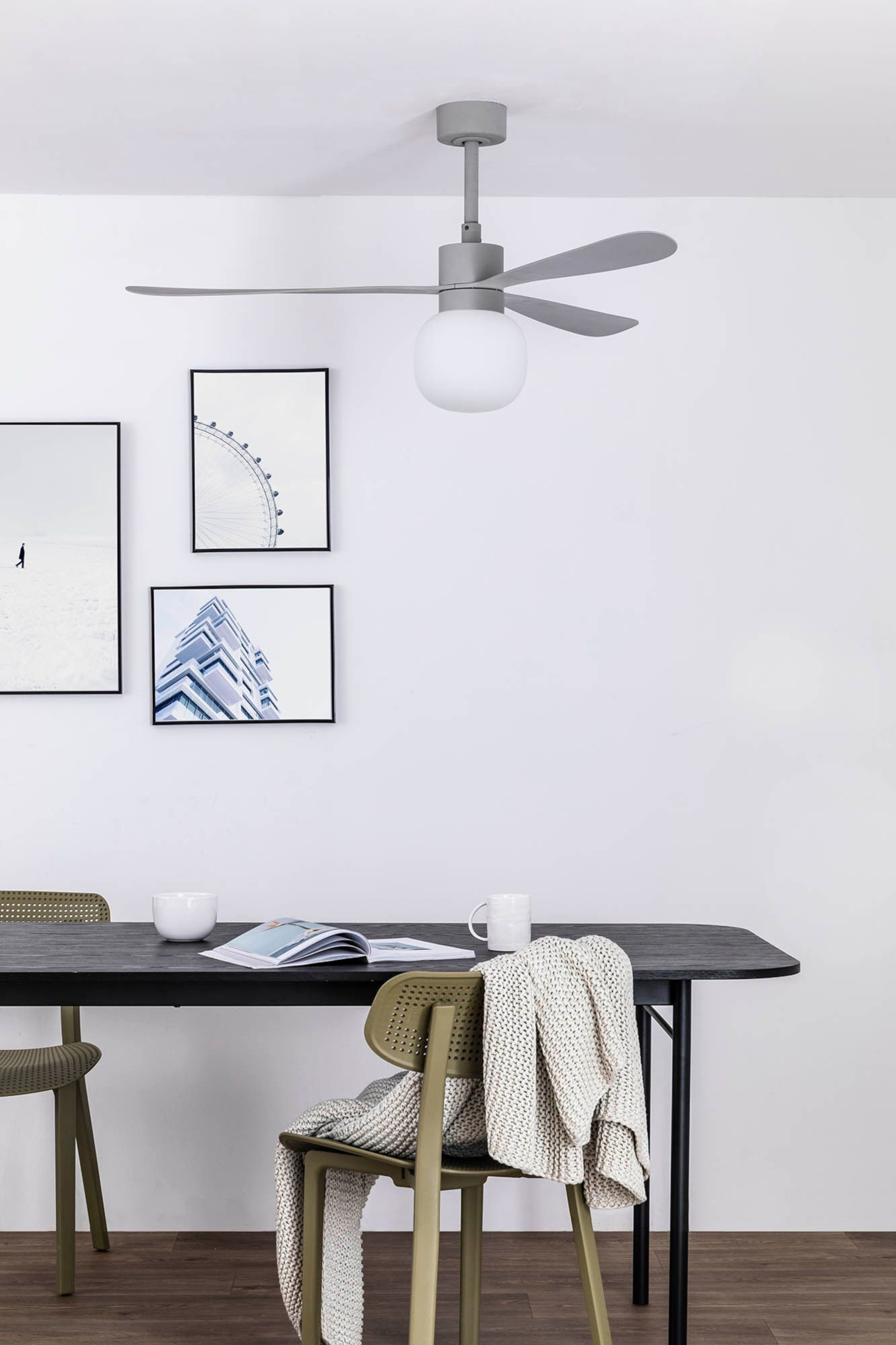 Ein Raum mit grauem Deckenventilator, Tisch, Stühlen und Bildern.