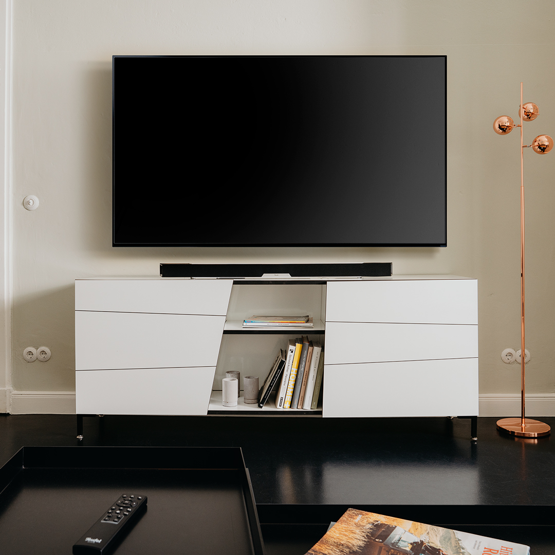 Fernseher auf weißem Schrank mit Soundbar montiert.