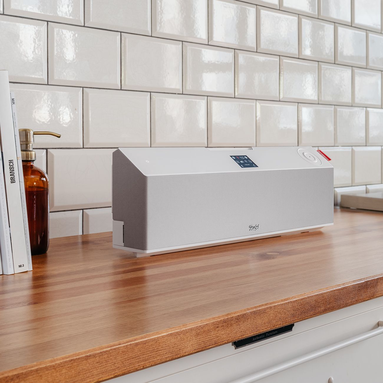 A modern kitchen with a white countertop, a speaker, and a brown glass bottle.