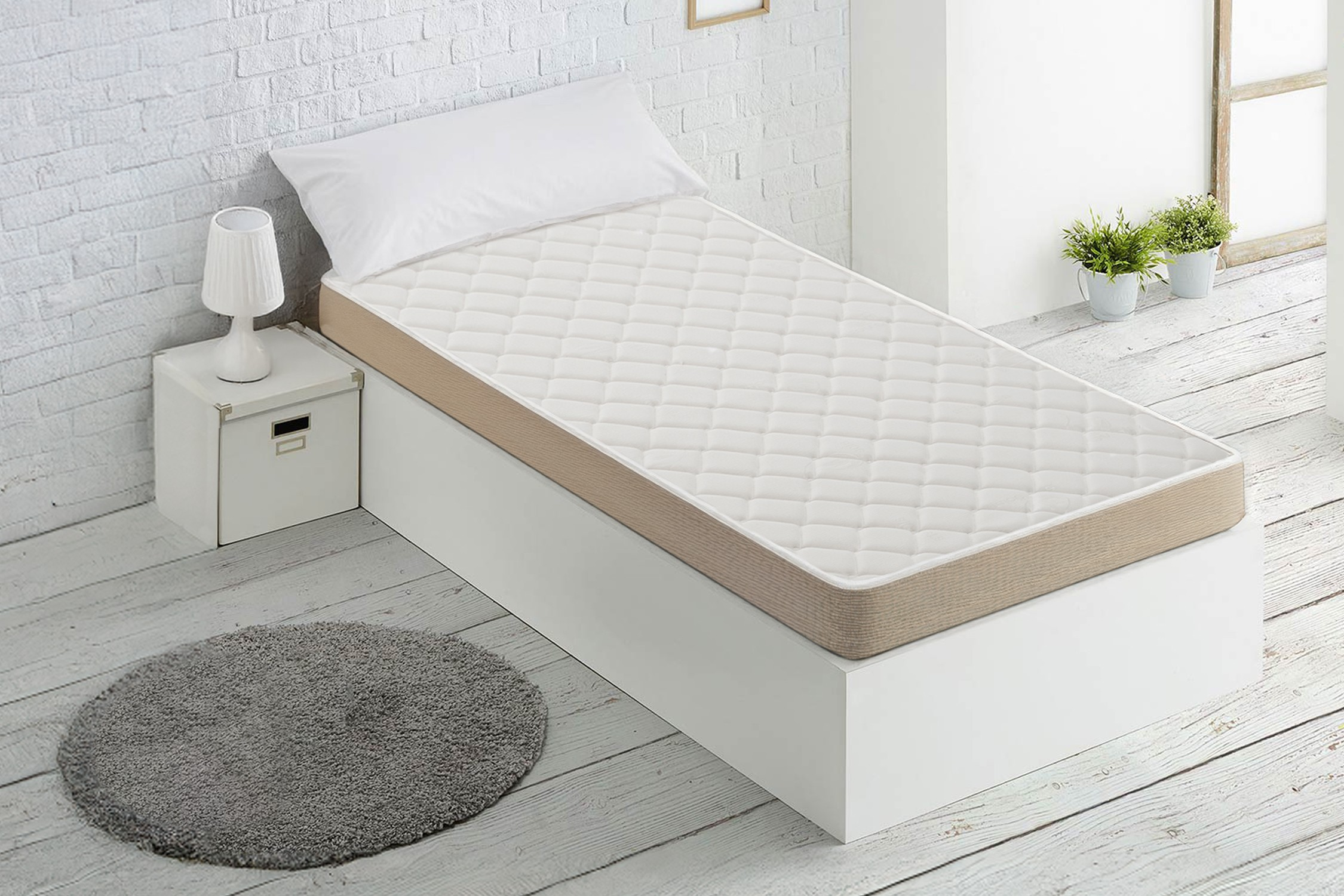 Un colchón blanco sobre una base blanca con almohada blanca, cerca de una mesita de noche.