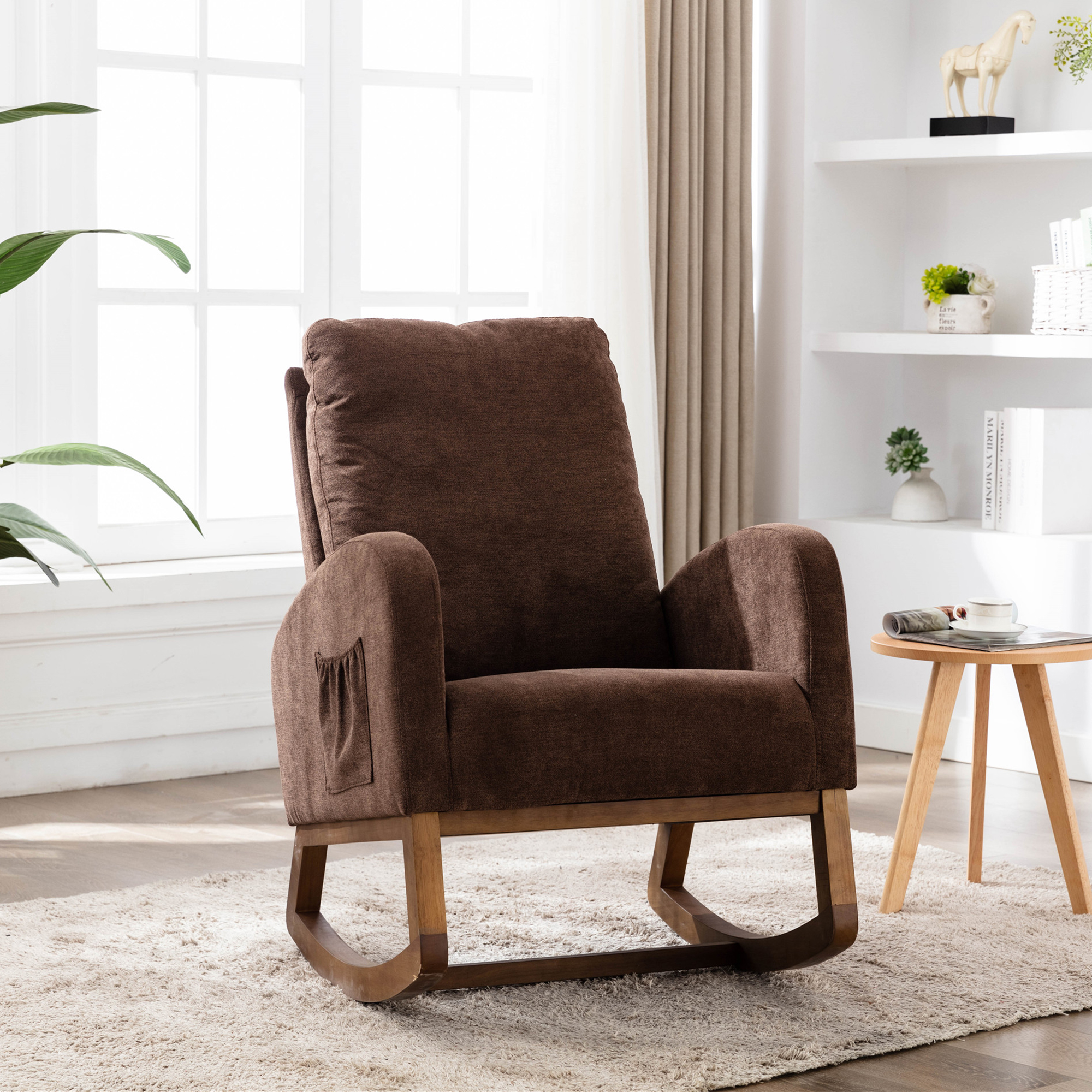 Ein brauner Schaukelstuhl in einem Wohnzimmer. Ein kleiner Tisch und Regale sind im Hintergrund.