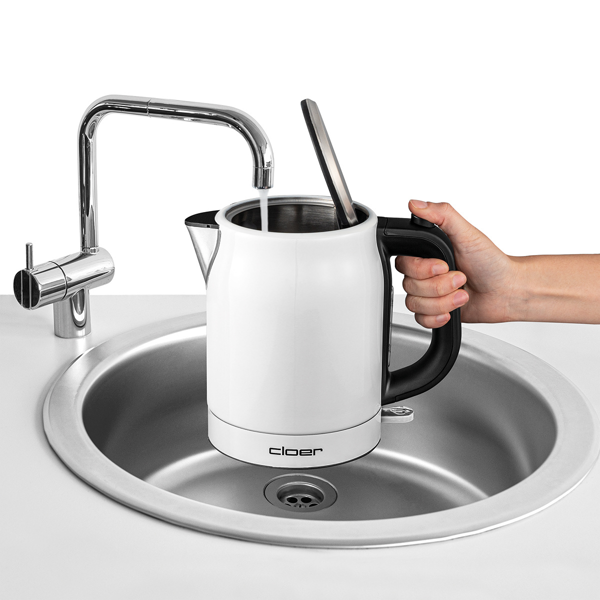 Biały czajnik napełniany wodą z kranu. Ręka trzyma czarny uchwyt. Widoczna marka Cloer.