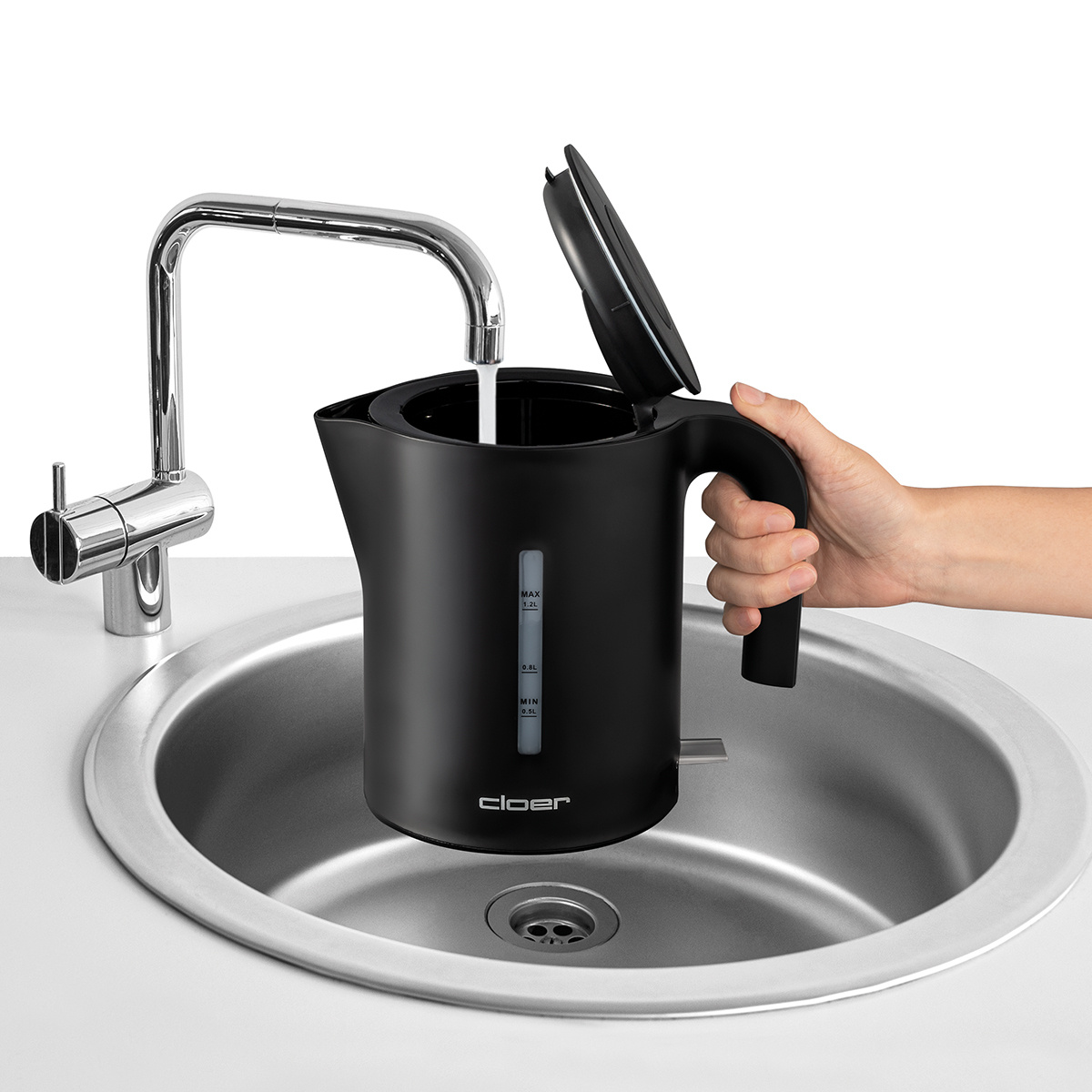 Ein schwarzer Wasserkocher wird in einem Edelstahlbecken mit Wasser aus einem Chromhahn gefüllt.