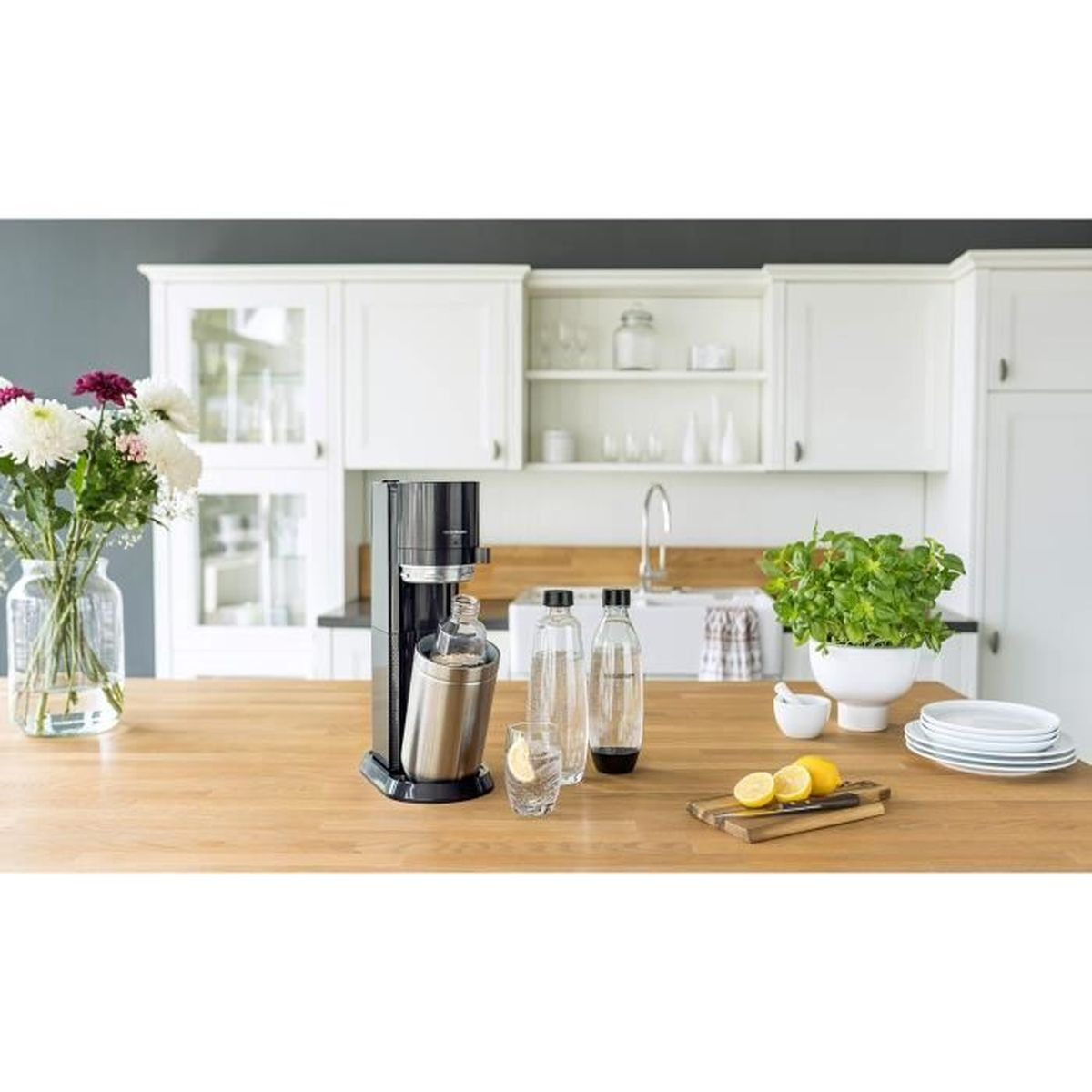 Scena di cucina. Macchina SodaStream sul bancone con bottiglie, limoni, fiori e piatti.