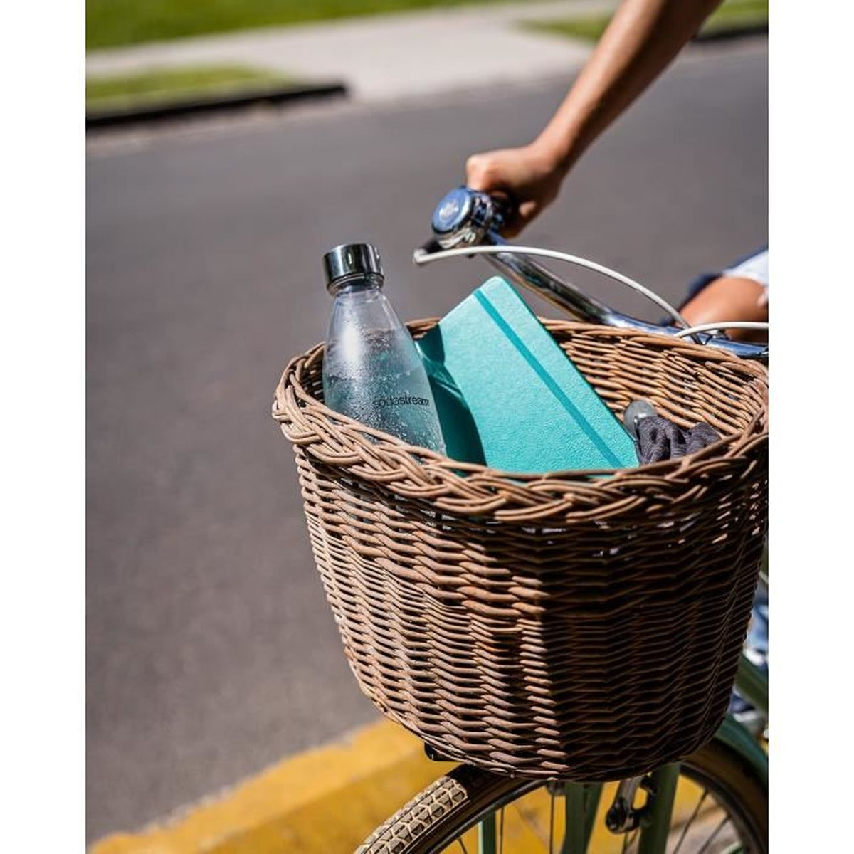 Persona in bicicletta con un cestino contenente una bottiglia d'acqua e un taccuino blu.