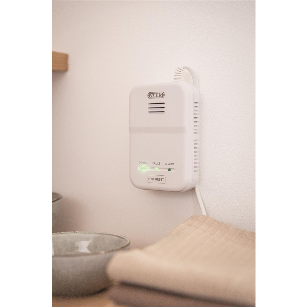 Weißer Rauchmelder an weißer Wand mit grünem Licht. Schalen und Tuch im Vordergrund.