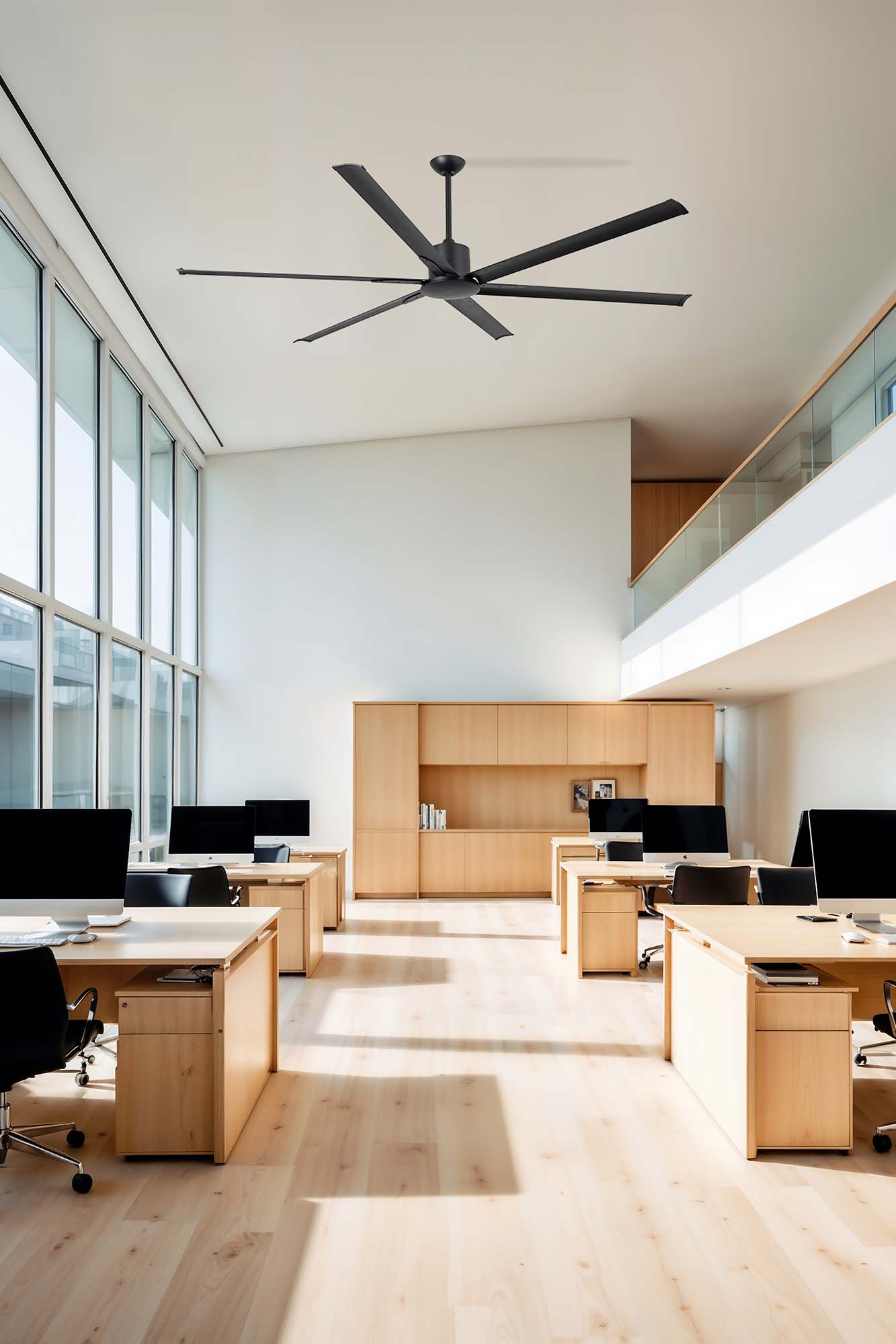 Büro mit Schreibtischen, Stühlen und schwarzem Deckenventilator. Große Fenster.