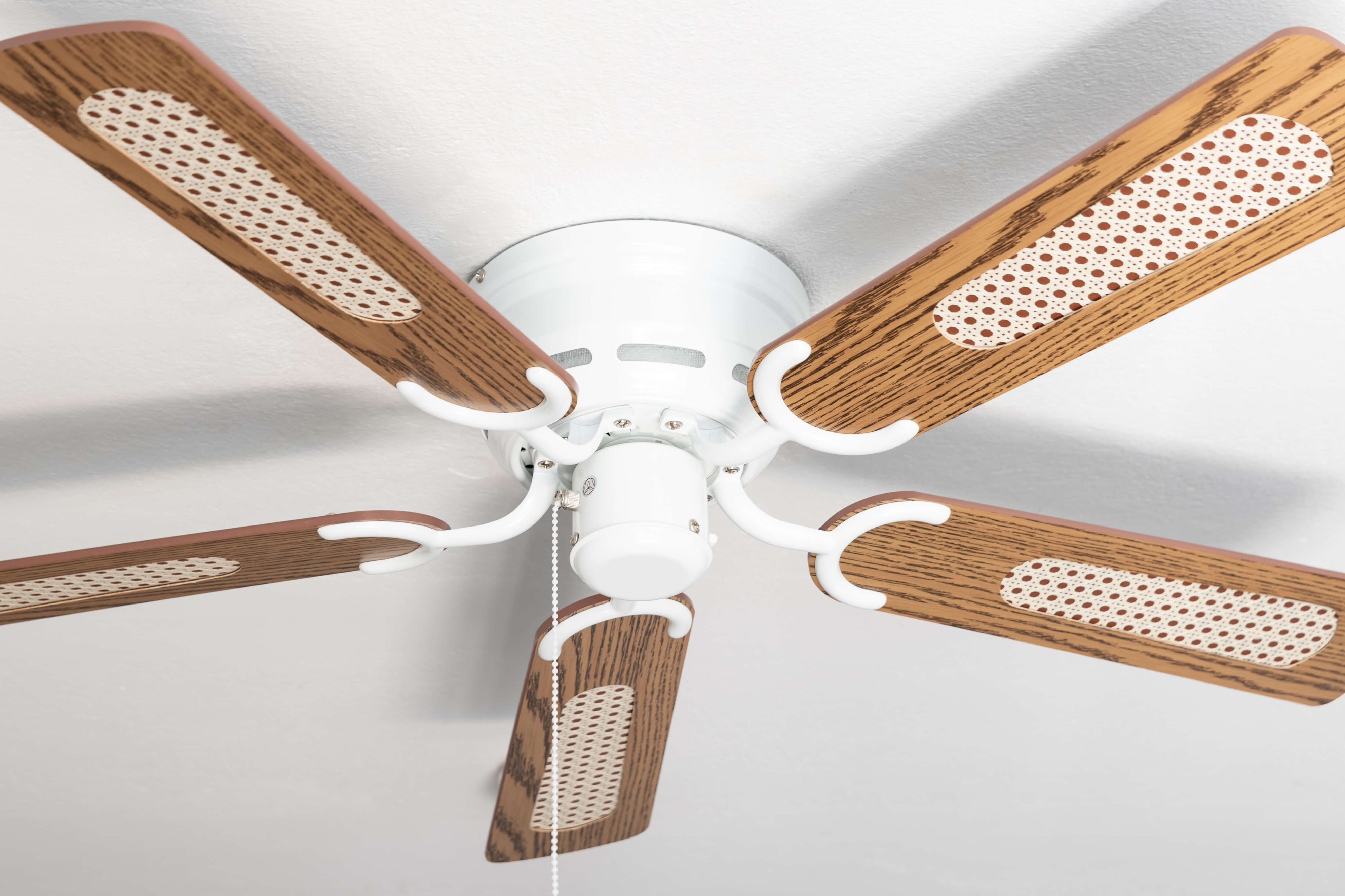 Deckenventilator mit braunen Flügeln und weißen Akzenten, an einer weißen Decke.