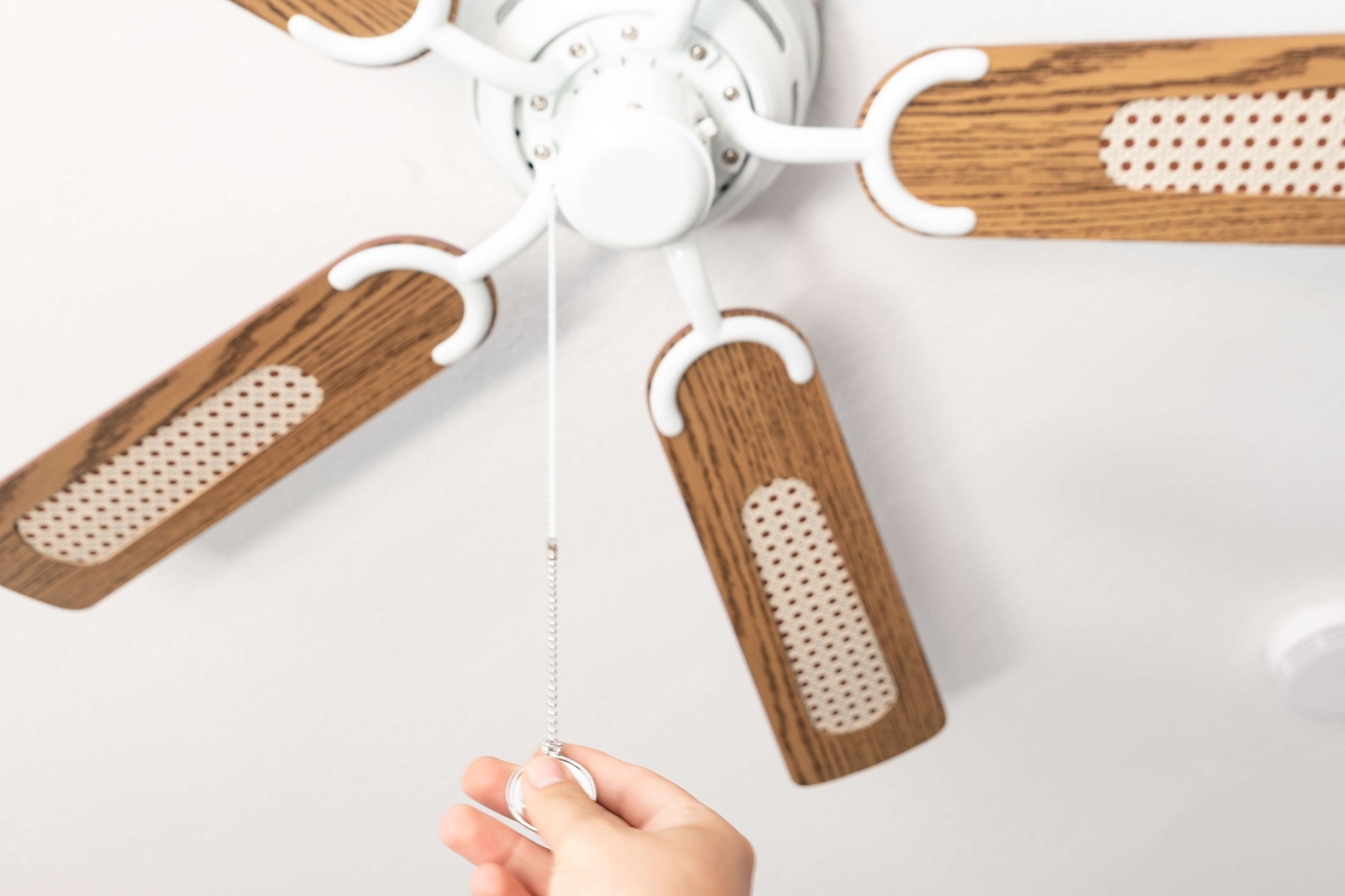 Eine Hand zieht an der Kette eines Deckenventilators. Der Ventilator hat Holzblätter.