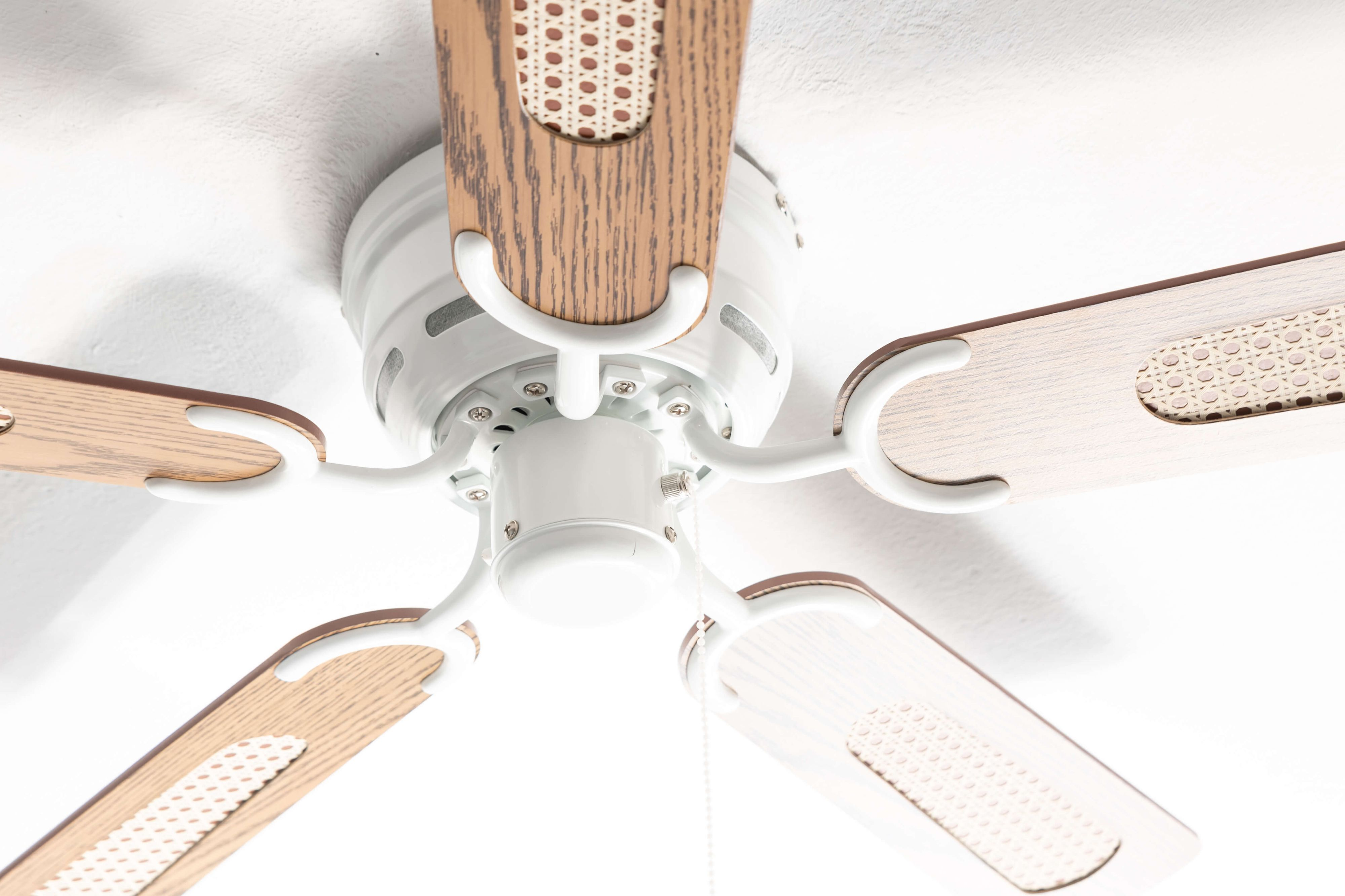 Deckenventilator von unten. Weißer Rahmen mit Holzflügeln und dekorativen Einsätzen. Weißer Hintergrund.
