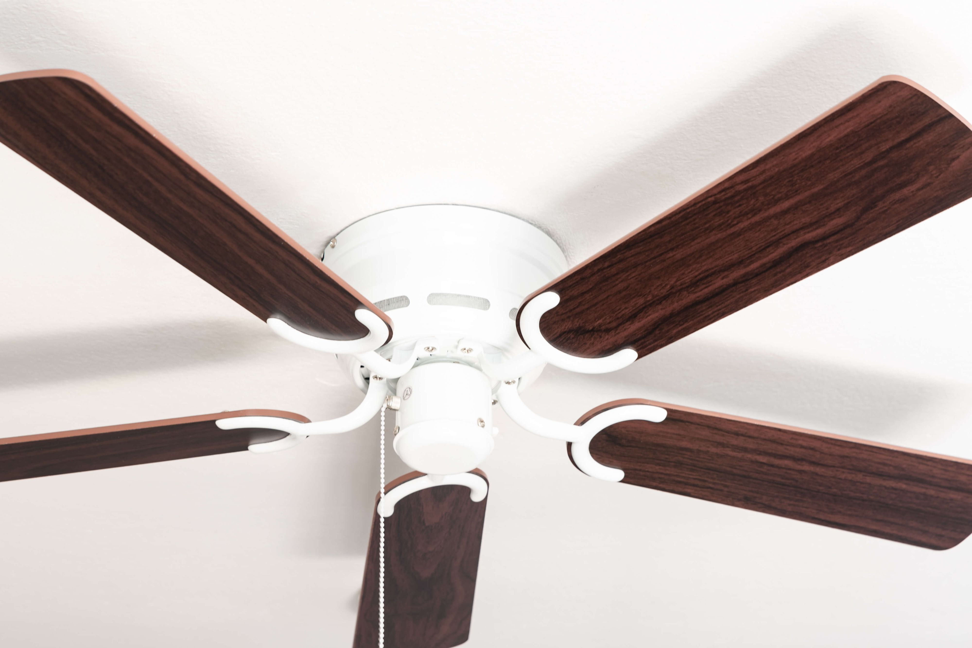 Deckenventilator mit fünf Holzoptik-Flügeln und einem weißen Motorgehäuse. An weißer Decke.