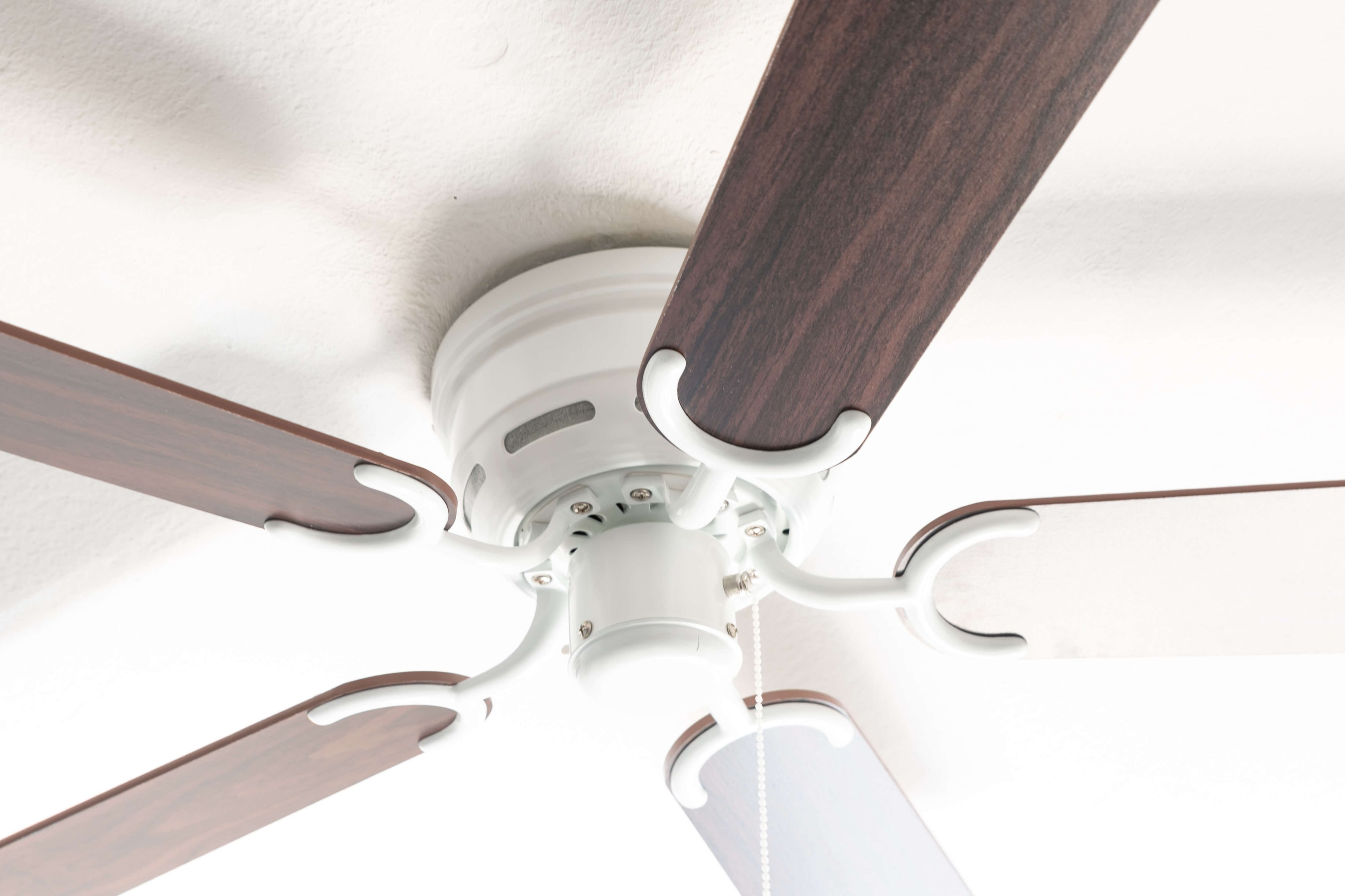 Ein weißer Deckenventilator mit braunen und weißen Holzblättern vor einer weißen Decke.
