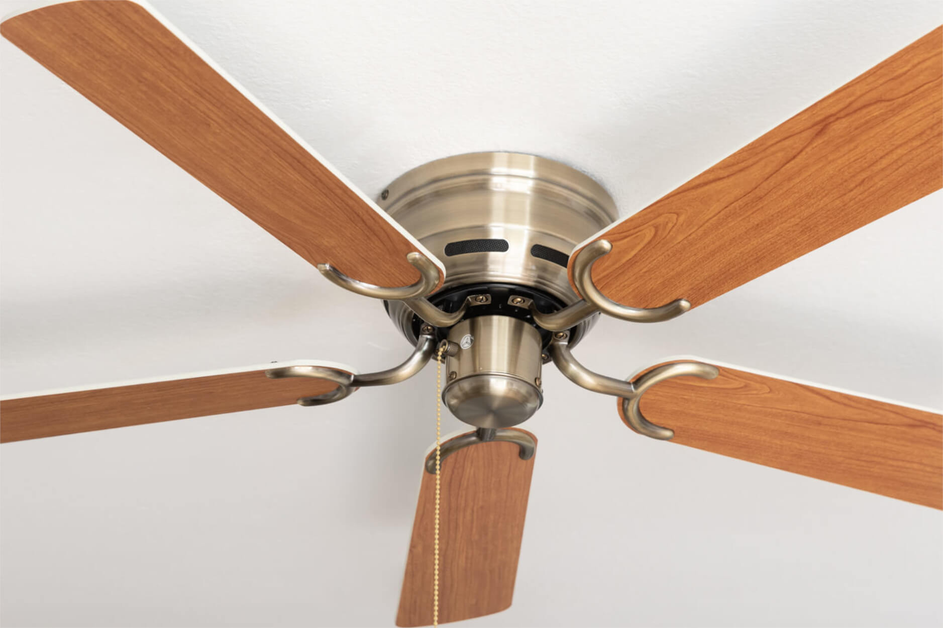 Deckenventilator mit braunen Holzblättern und messingfarbenem Motorgehäuse, vor weißer Decke.