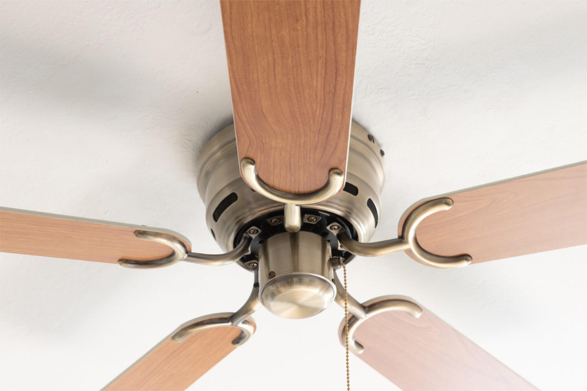 Ein Deckenventilator mit Holzblättern vor einer weißen Decke.
