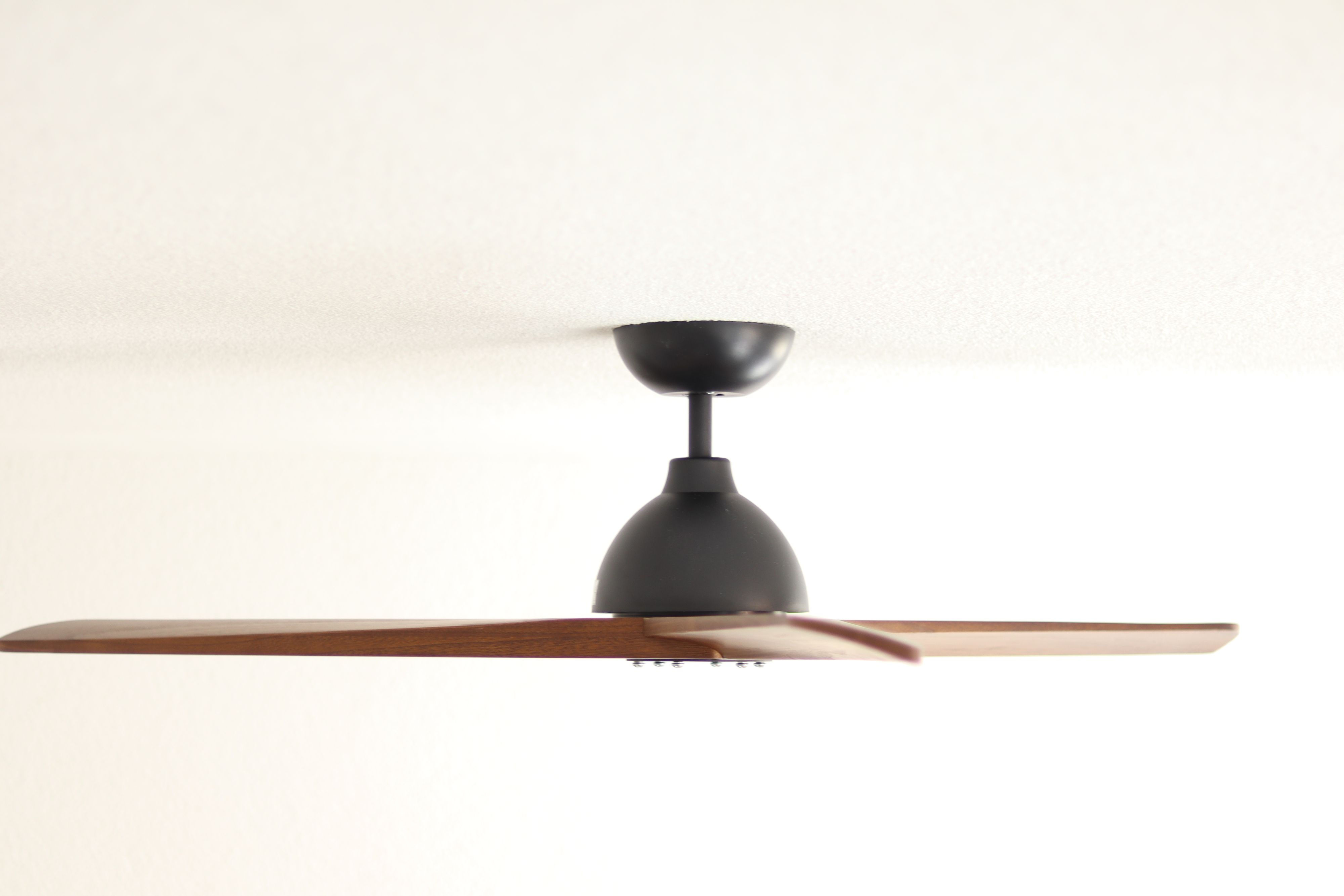 Ein schwarzer Deckenventilator mit braunen Flügeln ist an einer weißen Decke montiert.