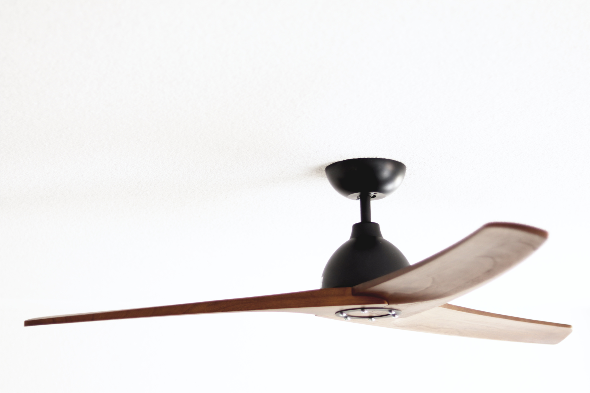 Deckenventilator mit drei Holzblättern an weißer Decke. Schwarzer Motor.